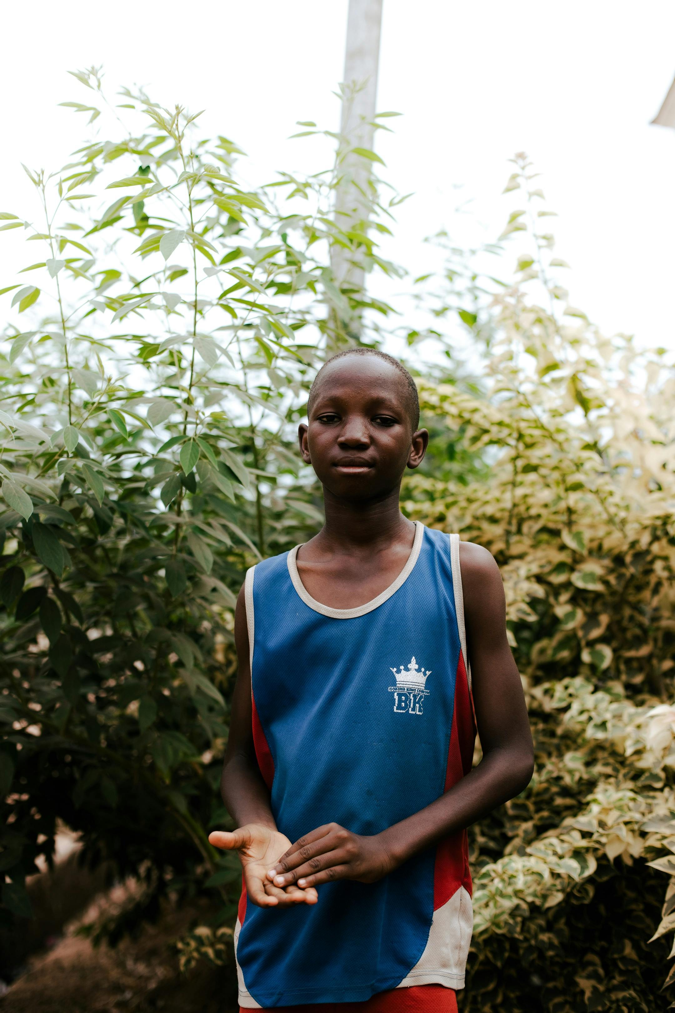bezplatná Mladý muž stojící venku obklopený bujnou zelení, oblečený v modrém tílku. Základová fotografie