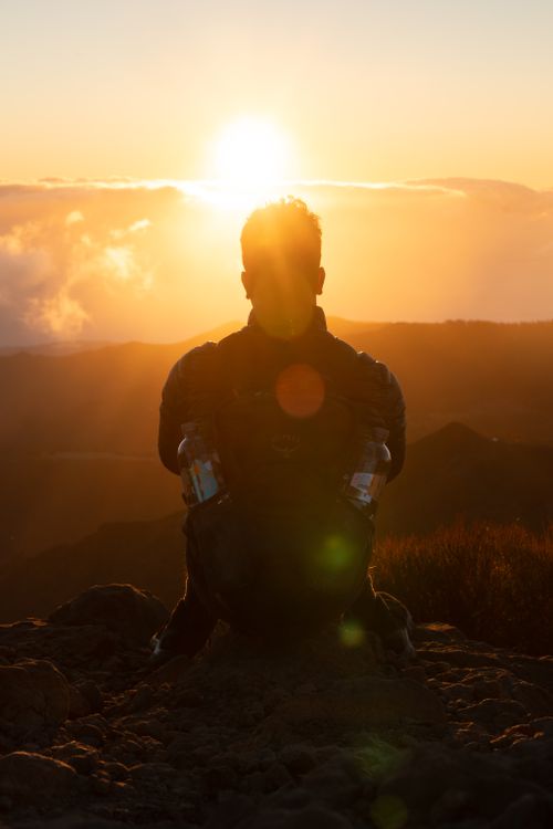 Free A silhouette of a person sitting on rocks, watching a vibrant sunrise over Madeira's landscape. Stock Photo