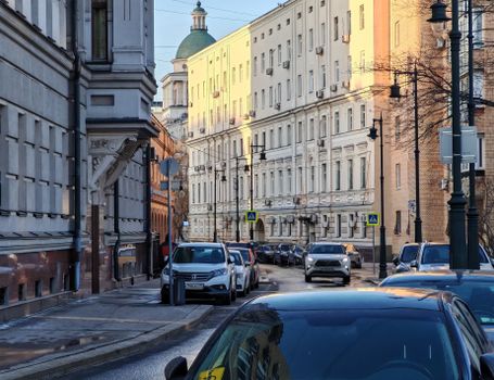 Charming street view in Moscow showcasing classic architecture and parked cars under warm sunlight.