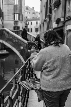 A street artist captures the essence of Venice's canals on canvas with a bridge in the background.