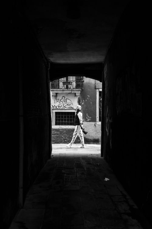 Free A person walks through a dark alley towards the light in Venice, Italy, creating a dramatic silhouette. Stock Photo