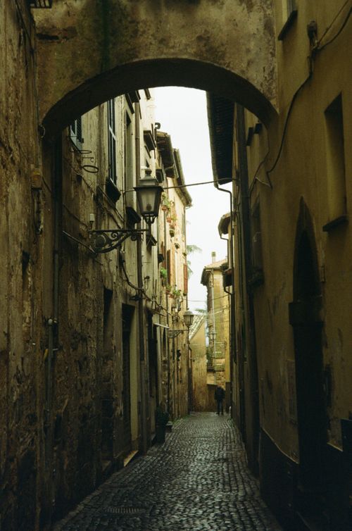 Free A picturesque narrow alleyway with cobblestone path and vintage buildings under an archway. Stock Photo