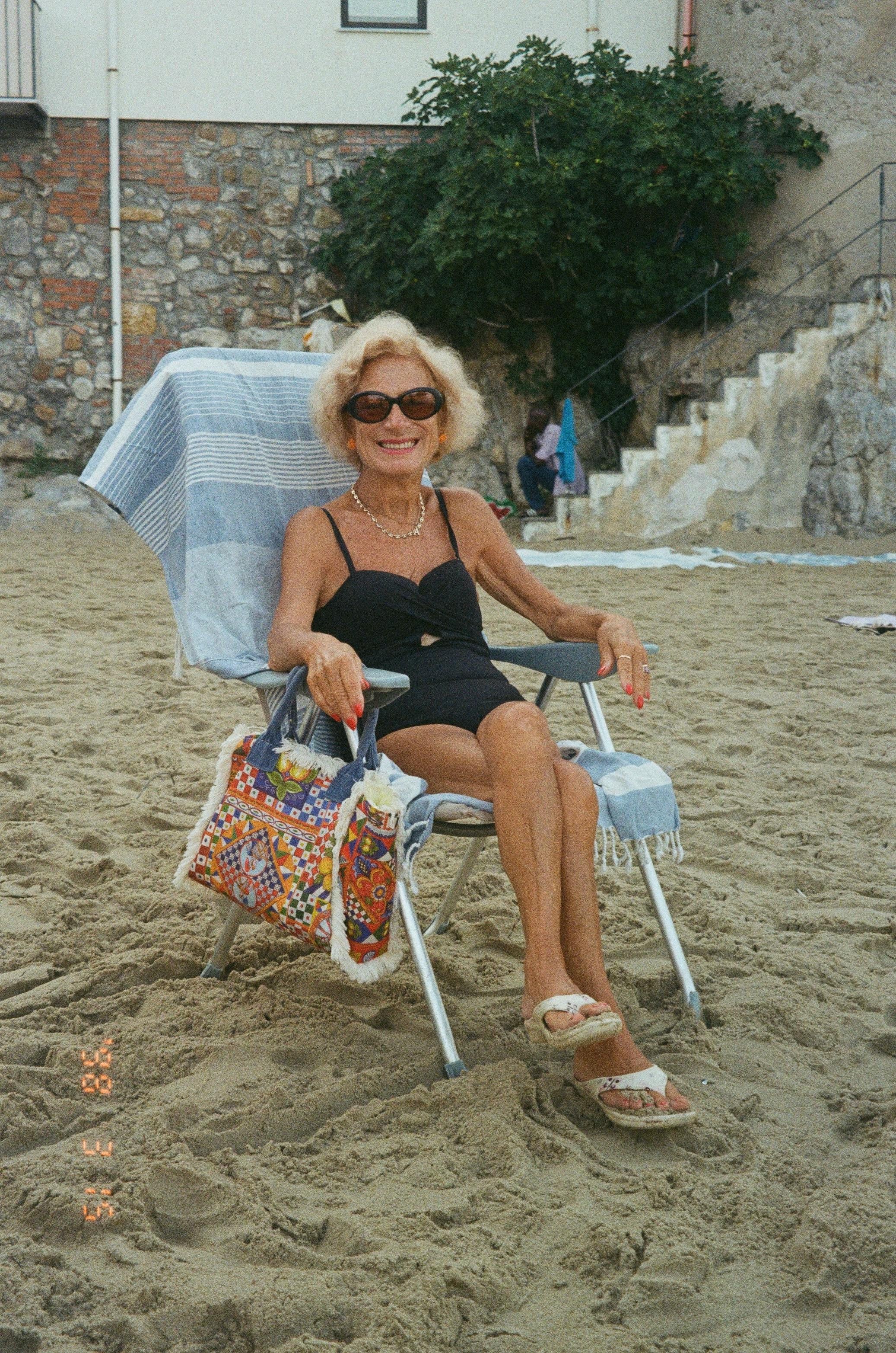 Senior woman enjoying a sunny day on a sandy beach in Italy, exuding elegance and relaxation.