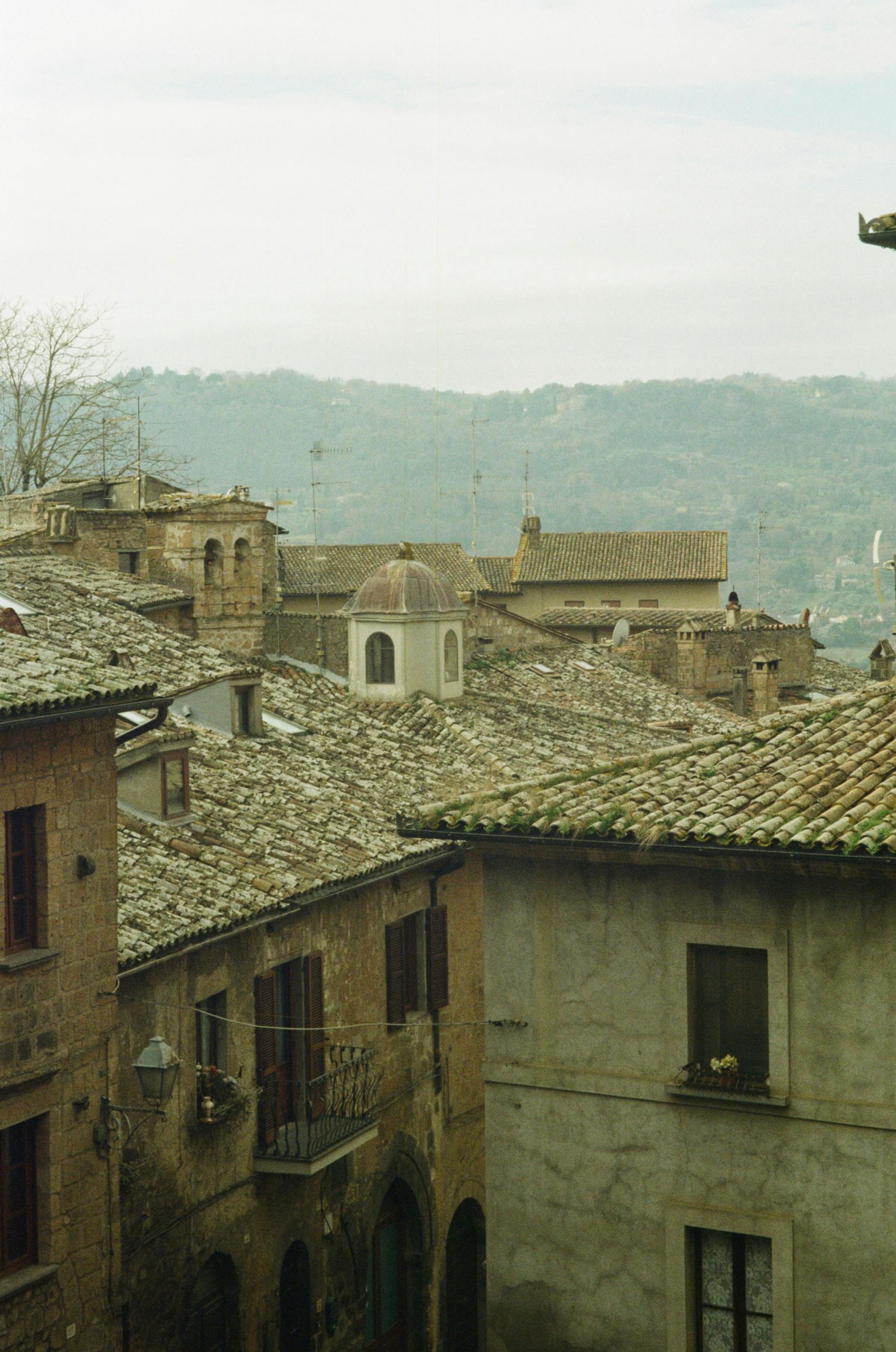 Ücretsiz Uzakta manzaralı tepelerin bulunduğu, şirin bir İtalyan köyünde rustik çatılar. Stok Fotoğraflar