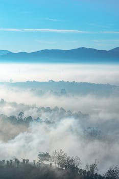 薄雾笼罩着山脉，在蔚蓝的天空下，呈现出一片宁静的景象