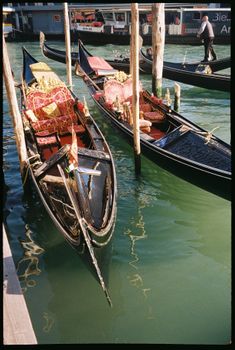 Colorful gondolas moored at a dock in a sunlit Venetian canal, Italy.