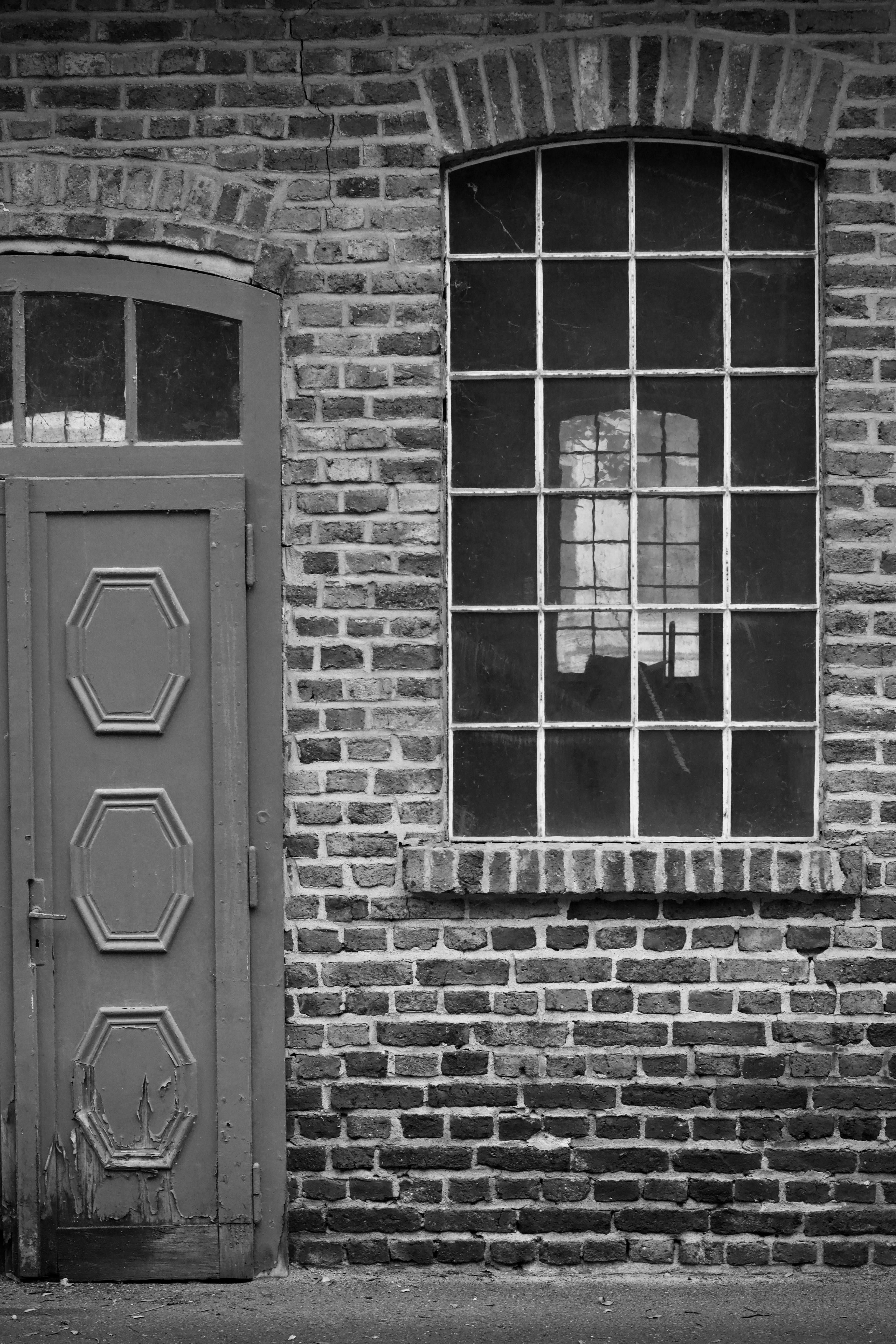 grátis Fotografia em preto e branco de uma parede de tijolos antiga com uma janela e uma porta ornamentada. Foto profissional