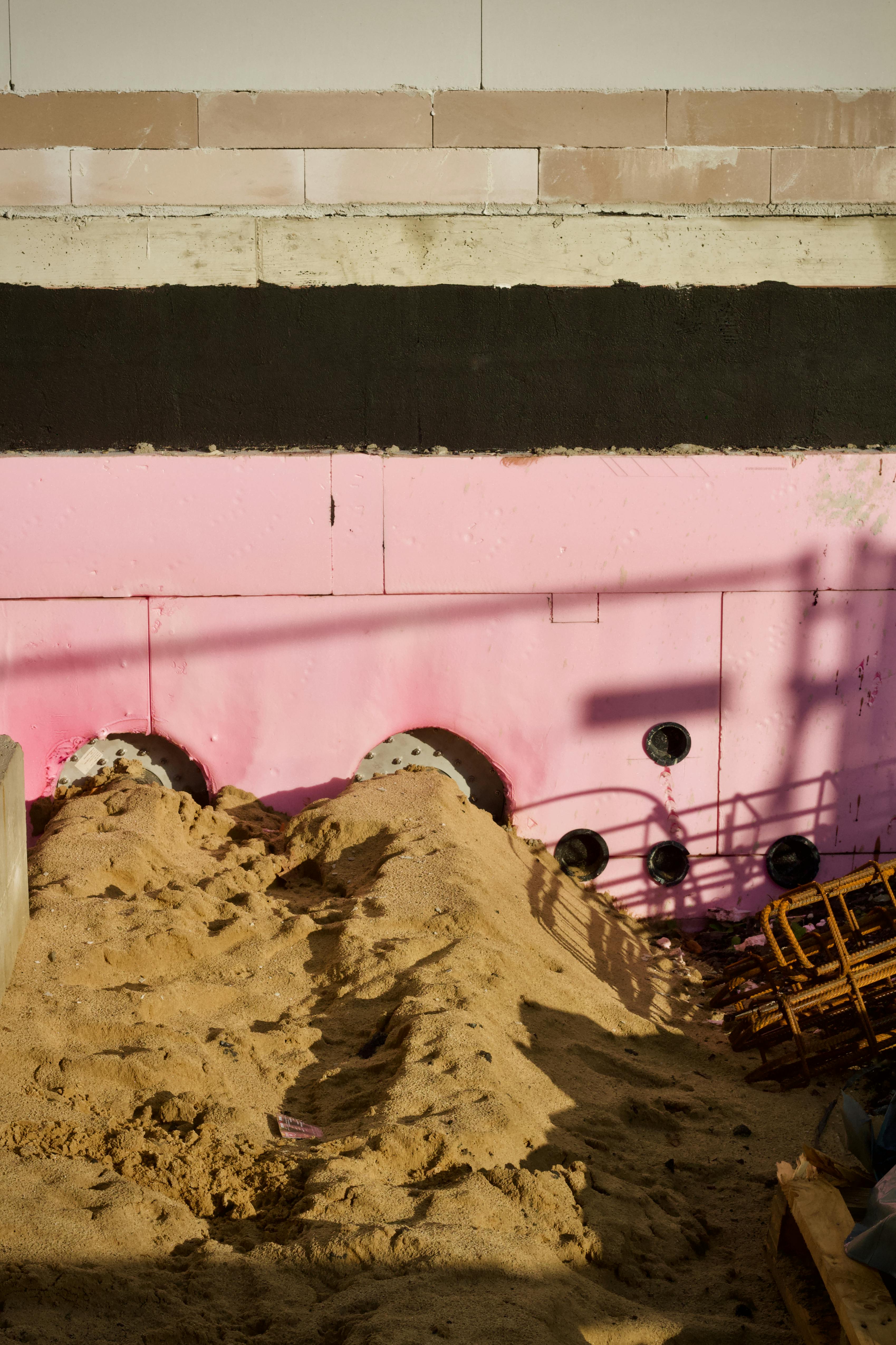 grátis Imagem de um canteiro de obras com painéis de isolamento rosa em um primeiro plano arenoso. Foto profissional