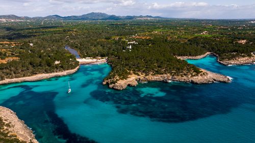 Free Aerial view of Mallorca's coastline with turquoise waters, cliffs, and lush greenery under a clear sky. Stock Photo