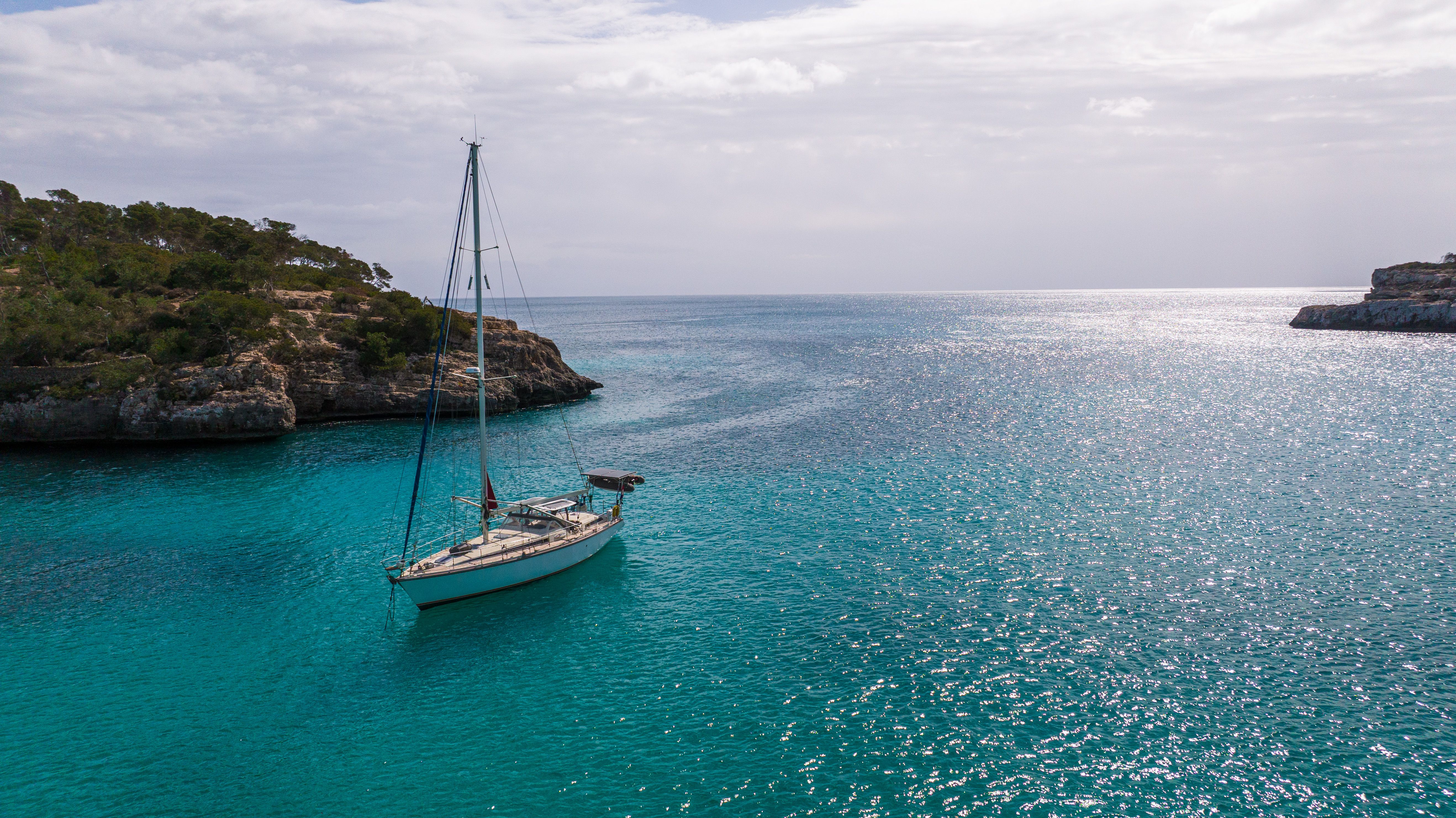 Amazing Barcelona Unique Private Luxury Sailing Tour (max 12 people) Review: A Luxurious Mediterranean Escape Worth Every Euro Review 2026 - A tranquil scene of a sailboat anchored in a beautiful cove in Mallorca, Spain, with clear blue waters.