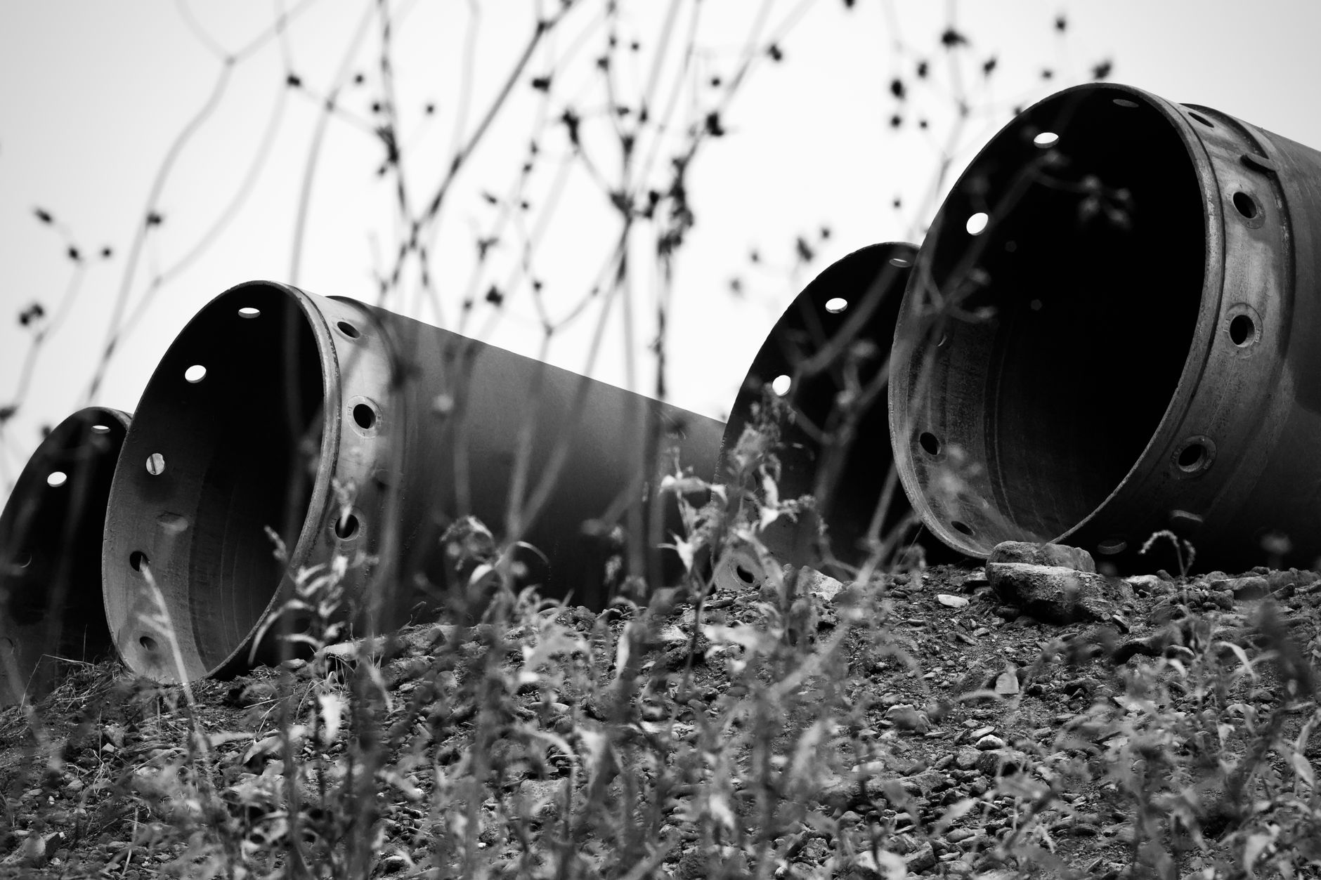 Monochrome image of large industrial pipes lying on a rocky outdoor landscape.