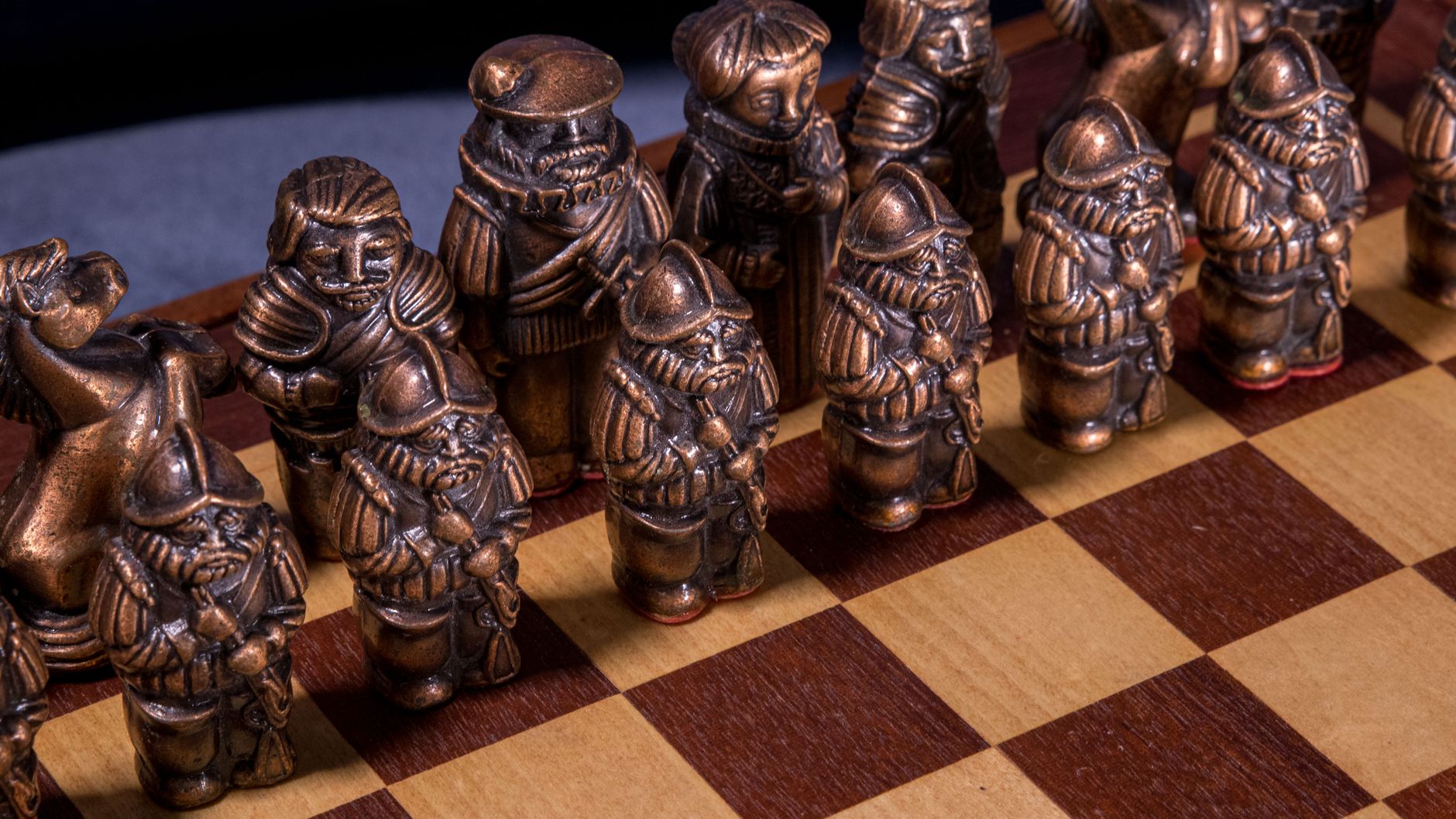 Detailed view of vintage copper-colored chess pieces with a medieval theme on a wooden chessboard.