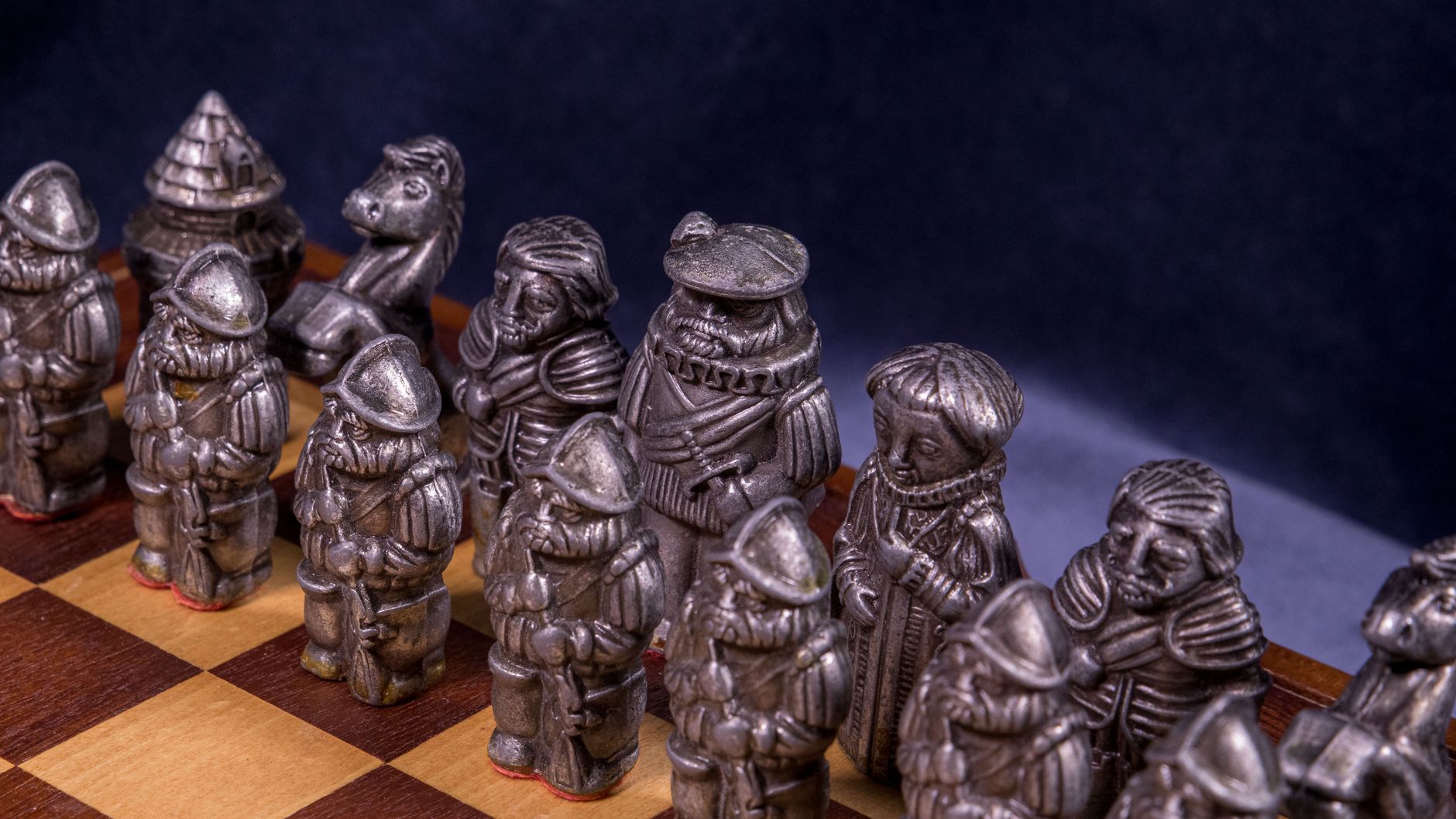 Close-up of intricately designed medieval-themed chess pieces on a wooden board under studio lighting.
