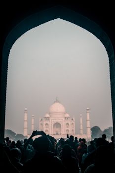 Silhouette of tourists under an archway viewing the iconic Taj Mahal at dawn in Agra, India.