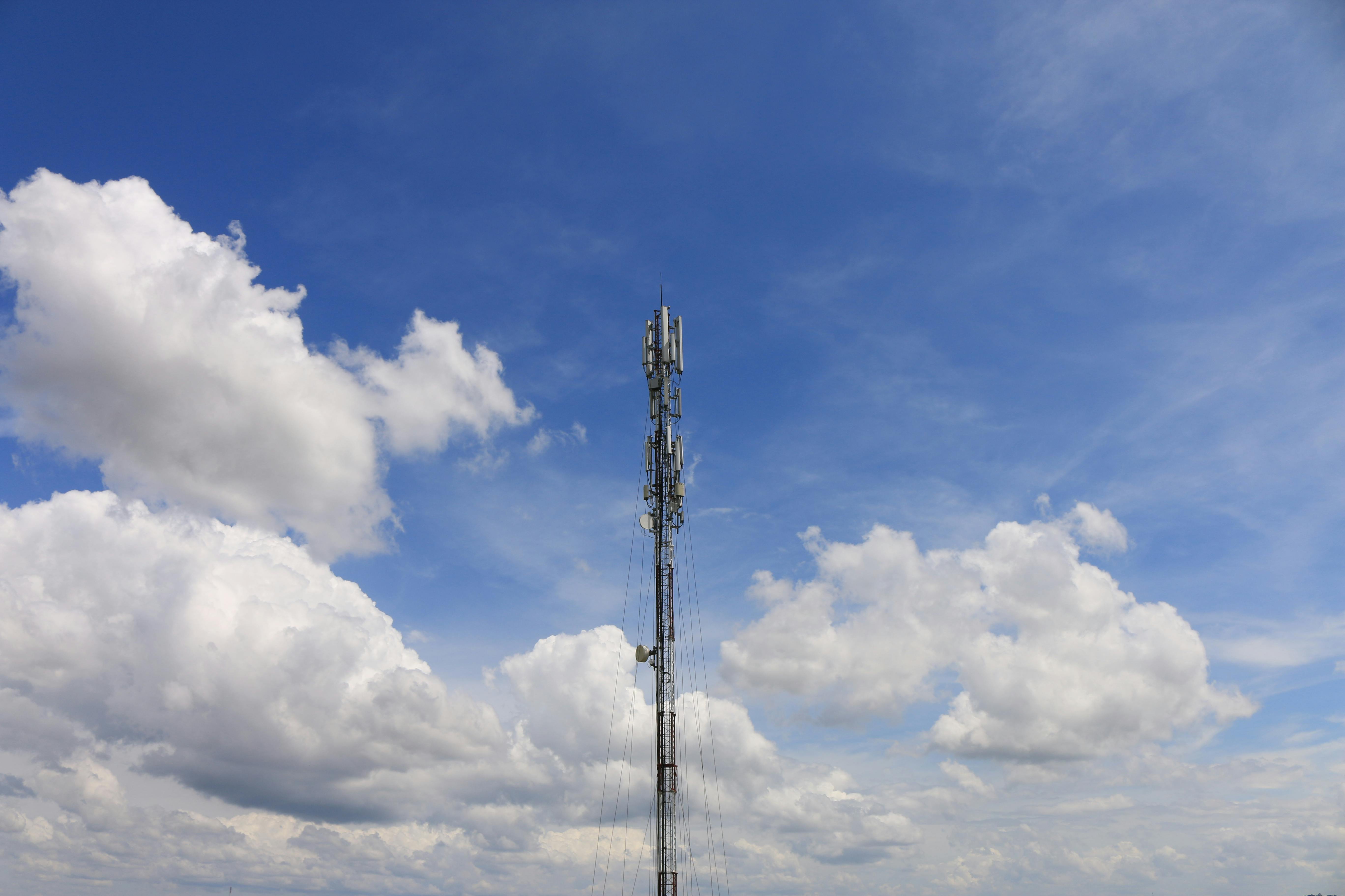 Communication tower standing against a bright, blue sky with fluffy white clouds, suggesting connectivity and technology.