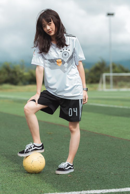Женщина в белой футболке и черных шортах, стоя на футбольном поле