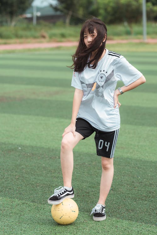 Mulher Vestindo Camisa Branca De Futebol E Shorts Pretos Enquanto Está De Pé No Campo De Futebol