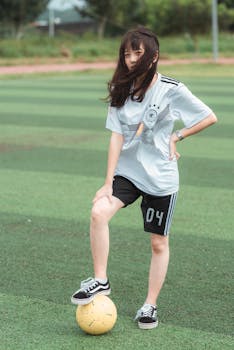 Teen girl in sportswear with a soccer ball on a field, showcasing casual style.