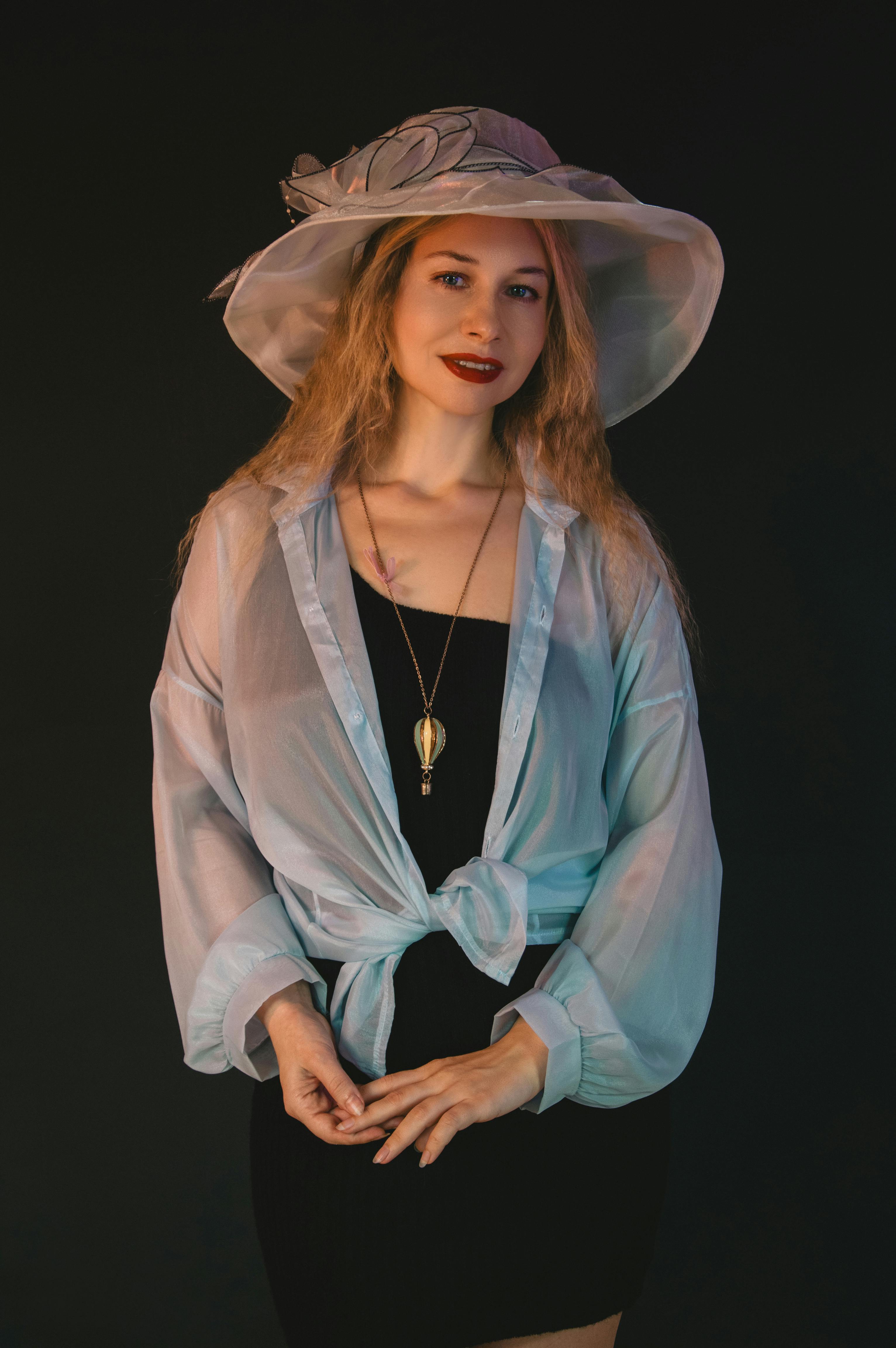 Kostenlos Porträt einer eleganten Frau, die einen schicken Hut und eine transparente Bluse über einem dunklen Kleid trägt. Stock-Foto