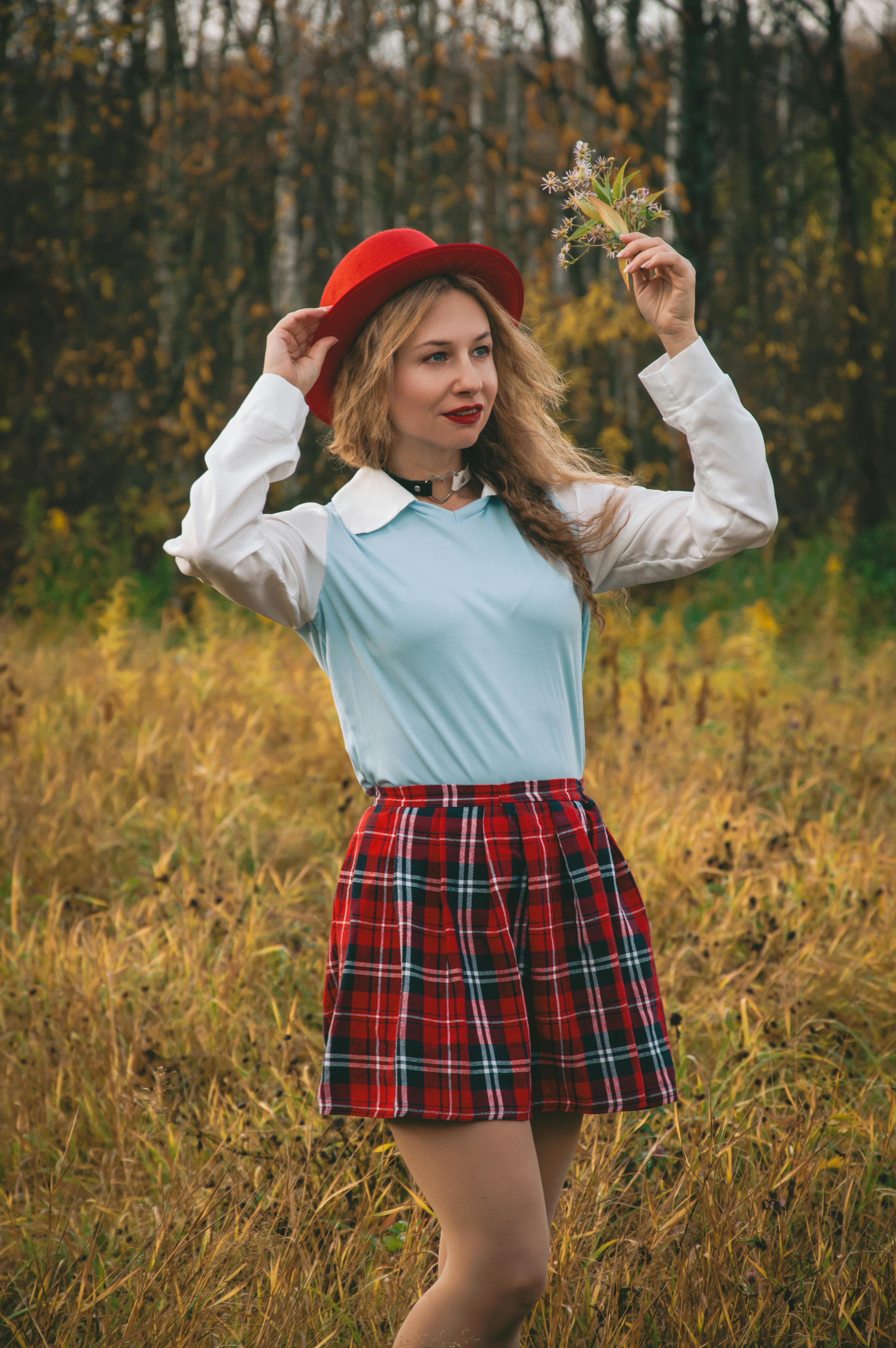 Gratis Donna alla moda con cappello rosso e gonna a quadri si gode la natura in un campo autunnale. Foto a disposizione