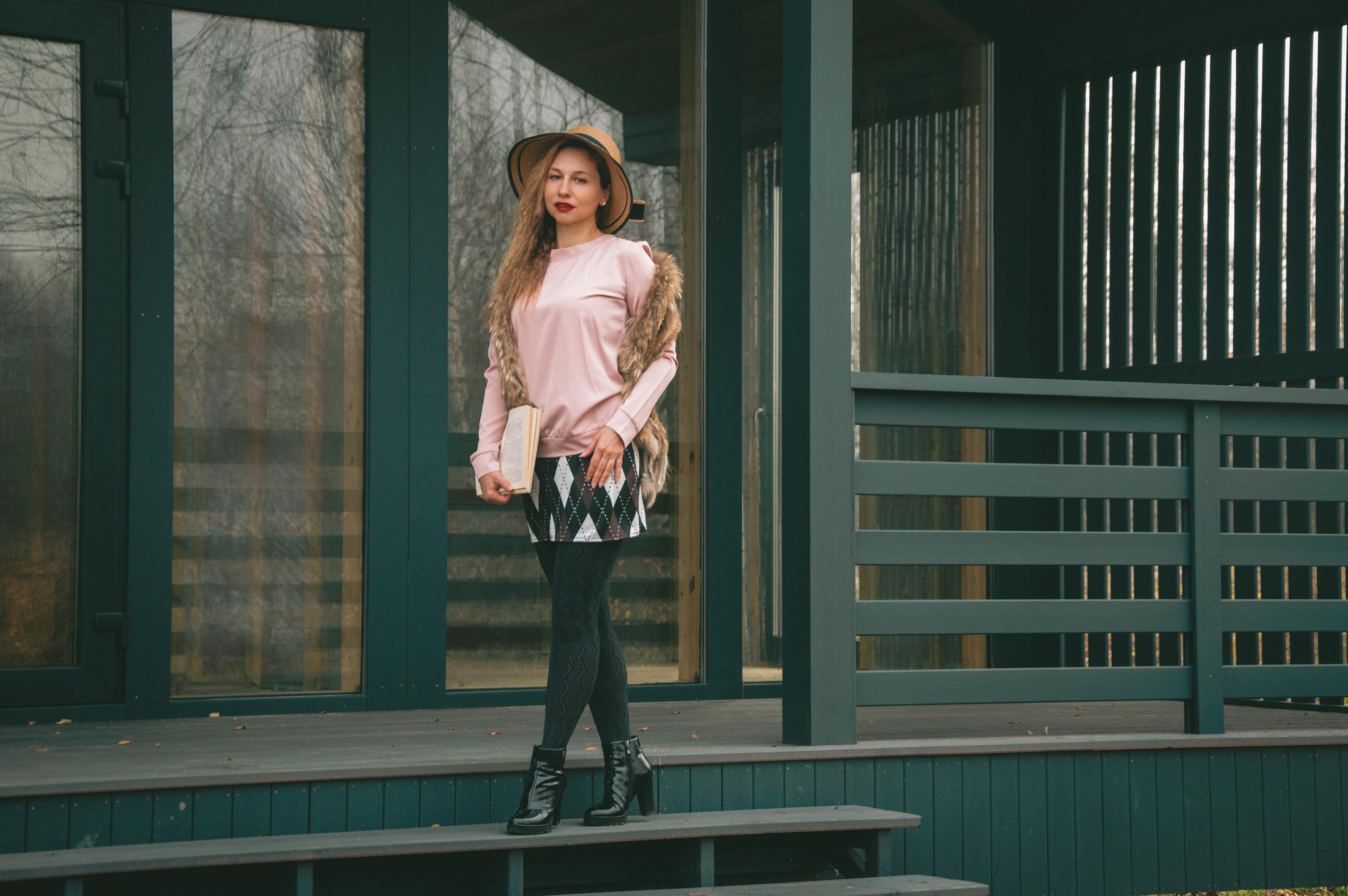 無料 ピンクの服と帽子を身に着けたスタイリッシュな女性が、屋外デッキで優雅にポーズをとっている。 写真素材