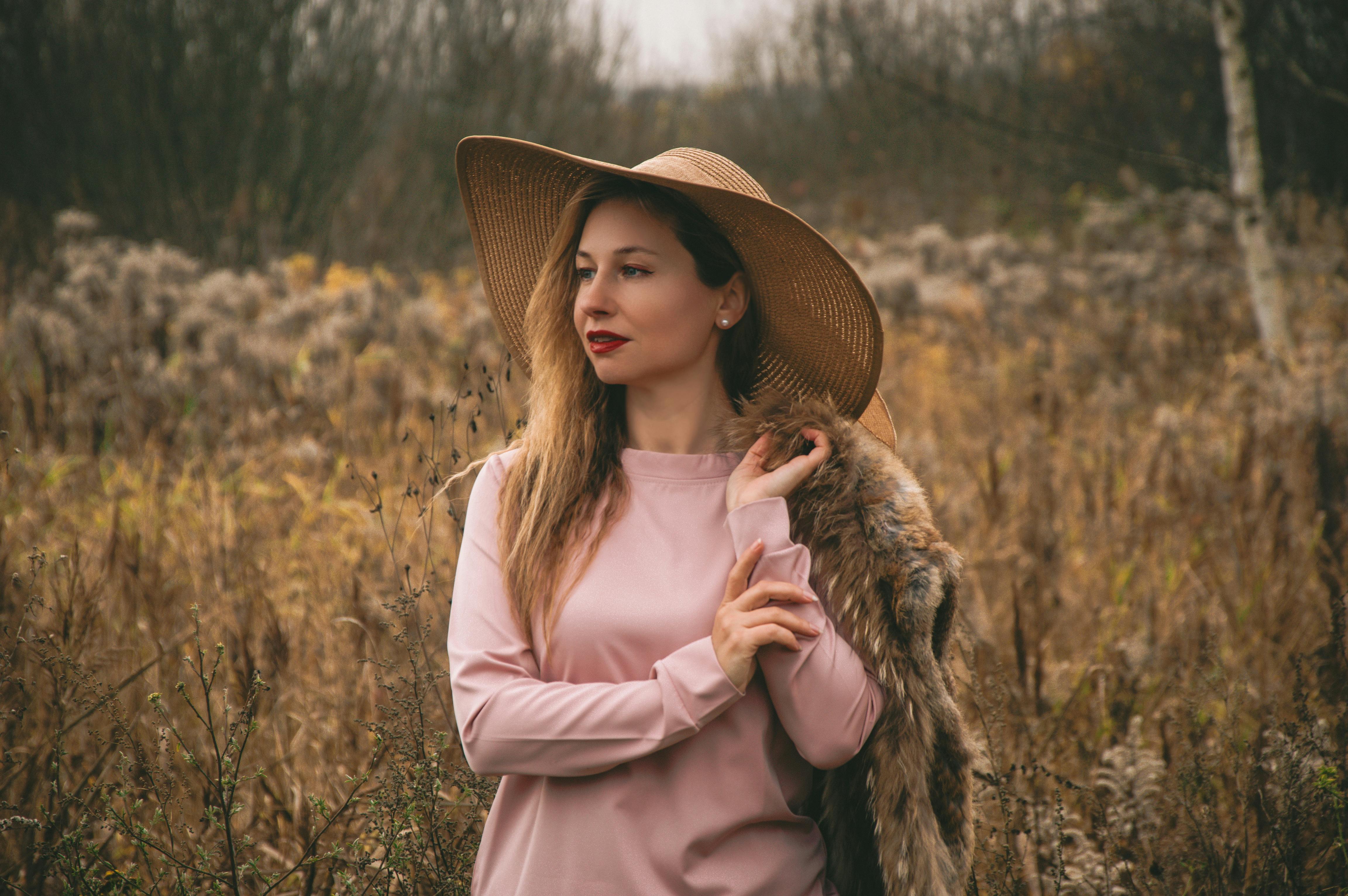 Ücretsiz Hasır şapka ve palto giymiş şık bir kadın, altın sarısı sonbahar tarlasında poz veriyor. Stok Fotoğraflar