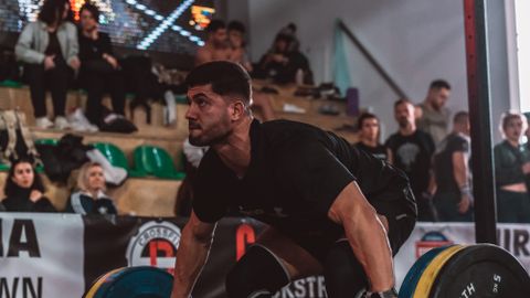 Young man performing deadlift in a crowded gym setting.
