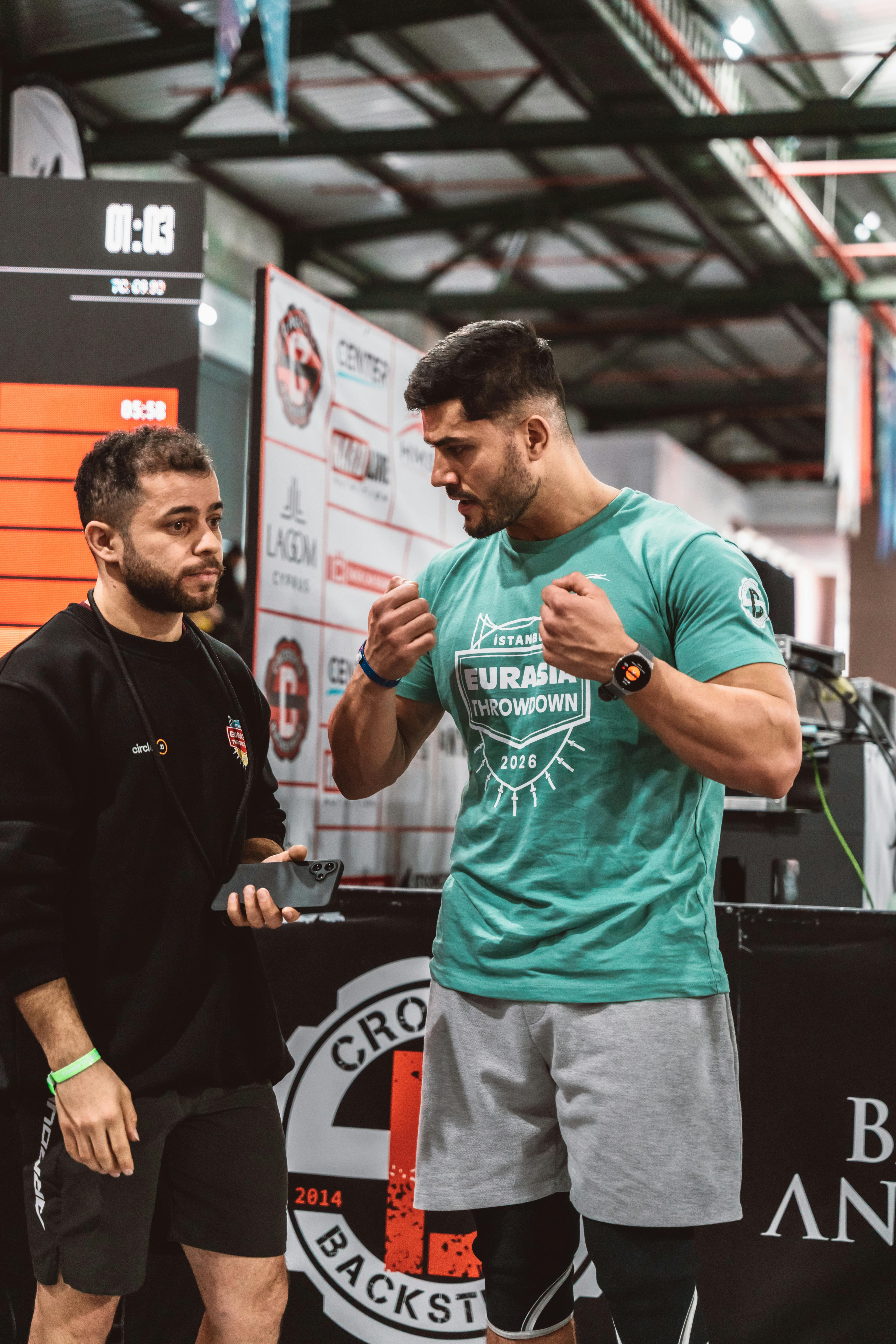 Two men engaged in conversation during an indoor fitness event with sports equipment around.
