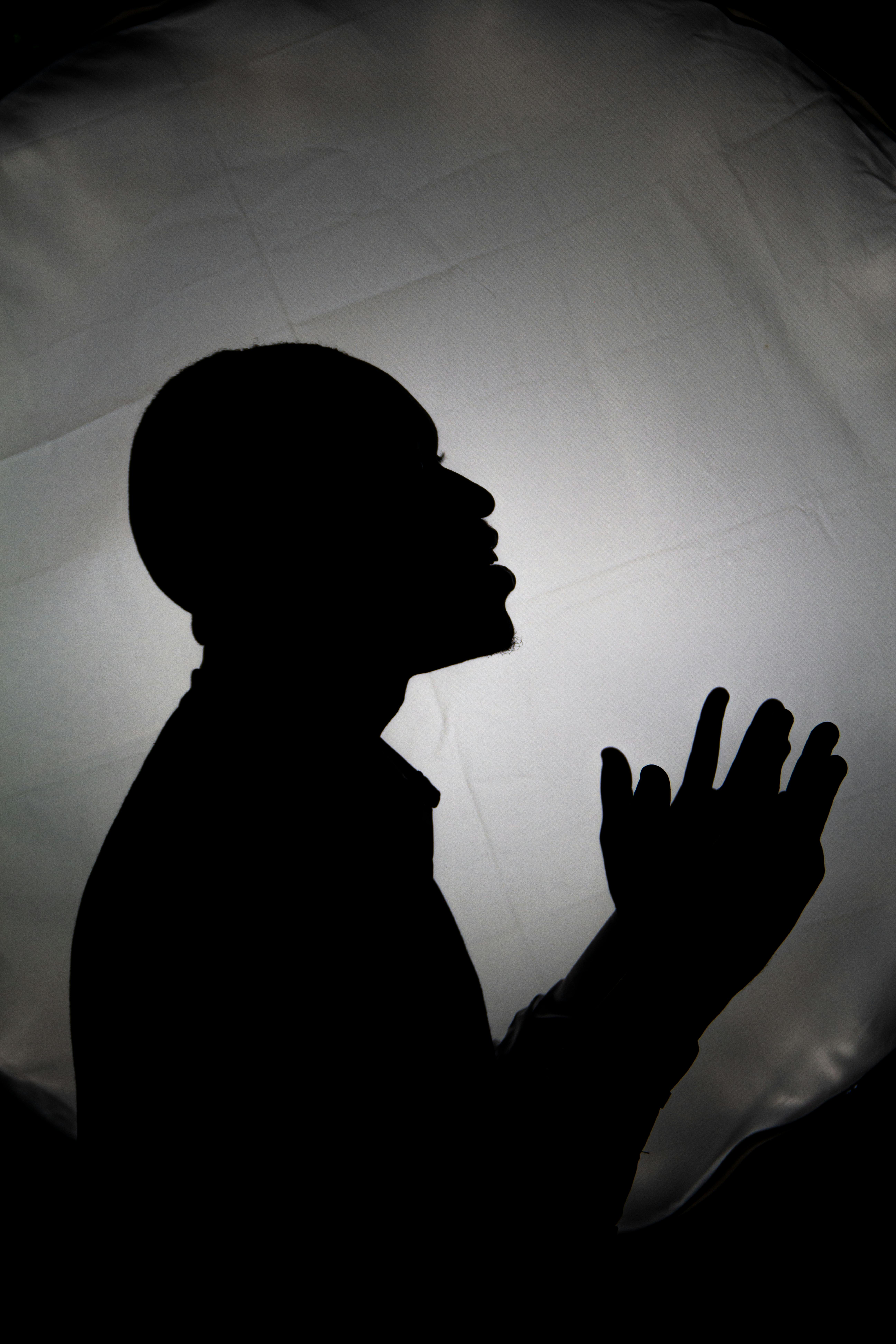 Bezpłatne Sylwetka modlącej się osoby na tle jasnego, delikatnego podświetlenia. Dramatyczna i spokojna. Zdjęcie z galerii