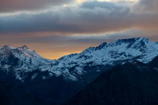 Dramatic view of snow-capped mountains under a colorful sunset sky in Korutany, Austria.