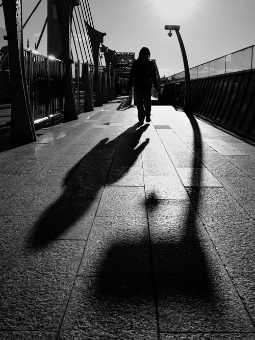 Free Moody black and white silhouette of a person walking with a long shadow on a bridge in Istanbul. Stock Photo