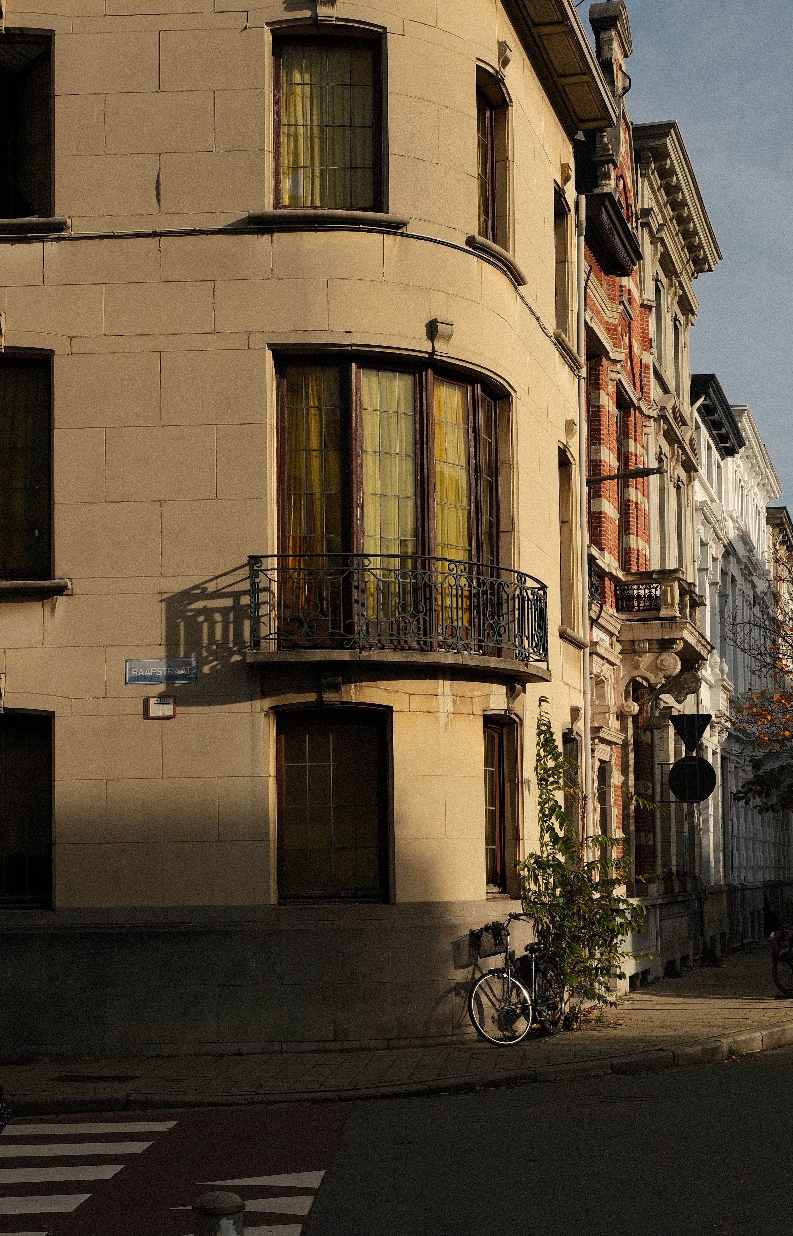 Sunset light casts a golden glow on a street corner in Antwerp, Belgium, with classic architecture and a bicycle.