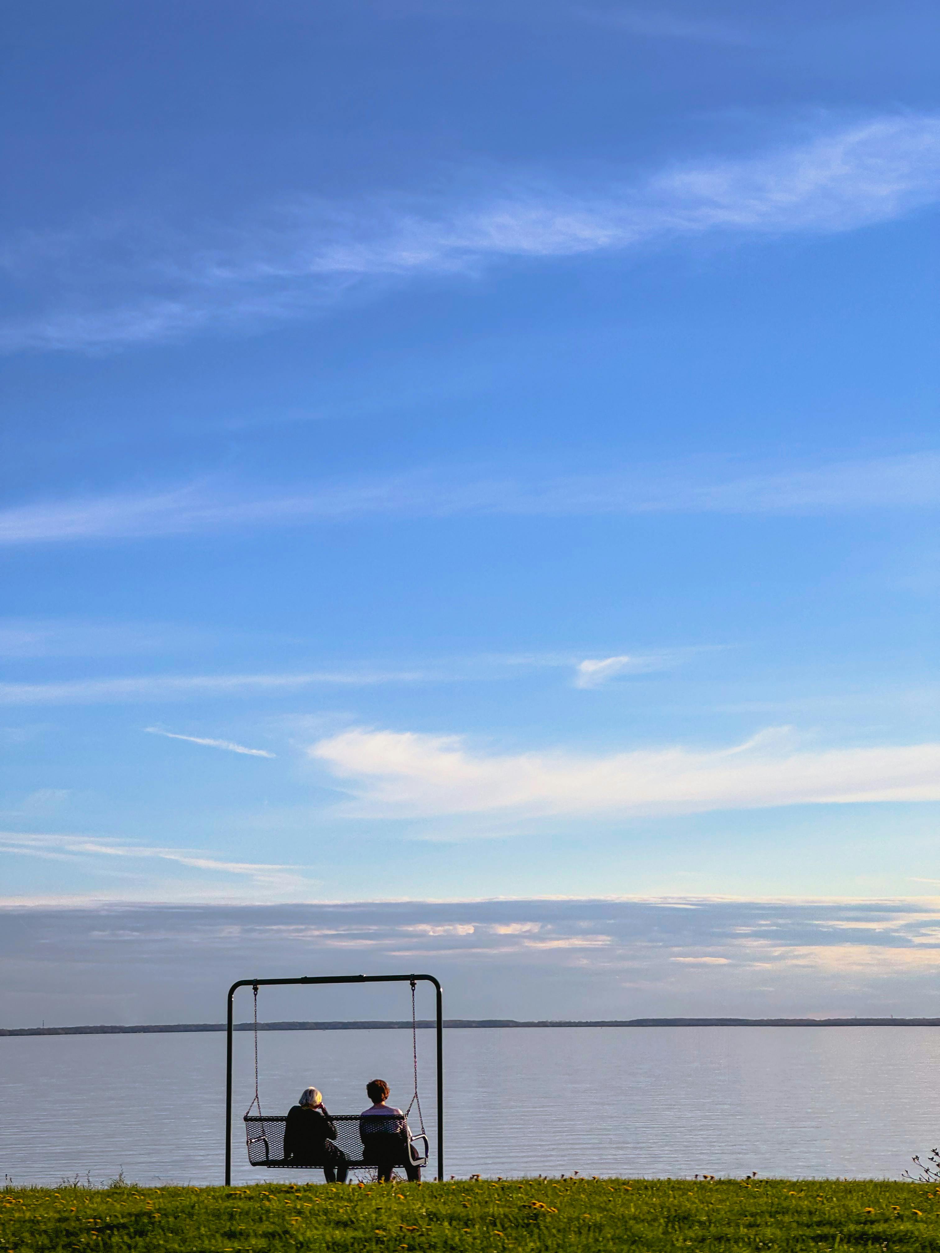 Ücretsiz Montreal'de, masmavi bir gökyüzünün altında, göl kenarında salıncakta oturan iki kişinin huzurlu manzarası. Stok Fotoğraflar