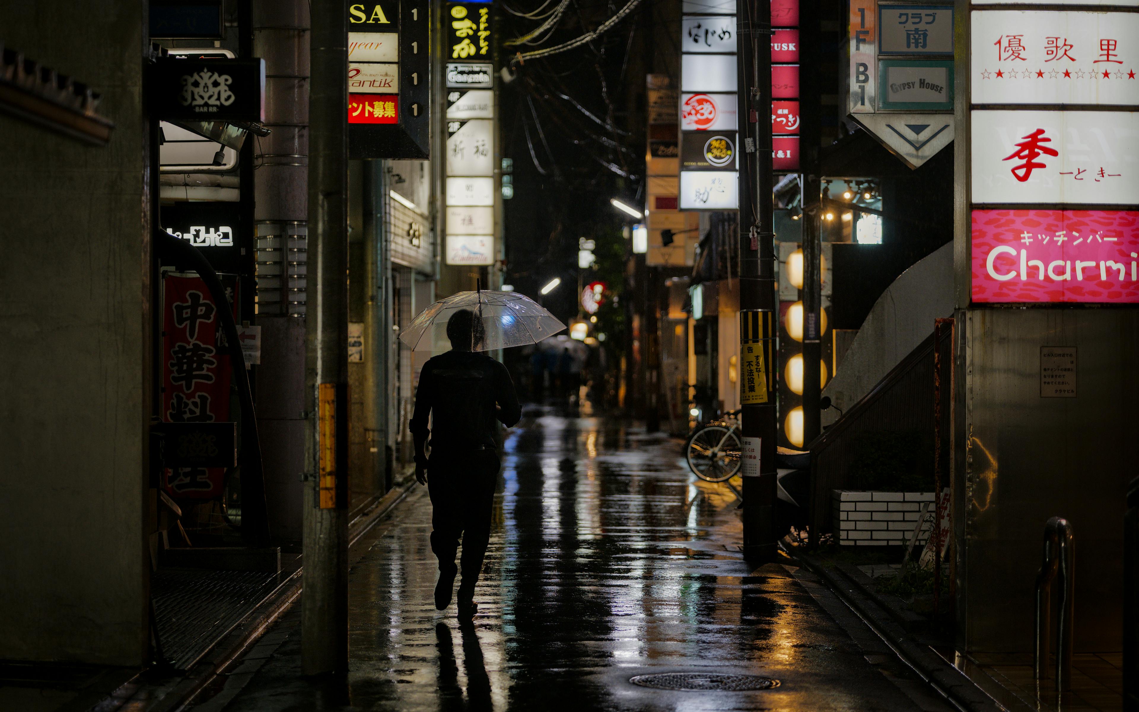 Gratuit O persoană se plimbă noaptea cu o umbrelă pe străzile ude, mărginite de reclame luminoase, în Kyoto. Fotografie de stoc
