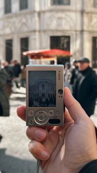 Close-up of an old camera screen showing a historic building with blurred pedestrians in the background.