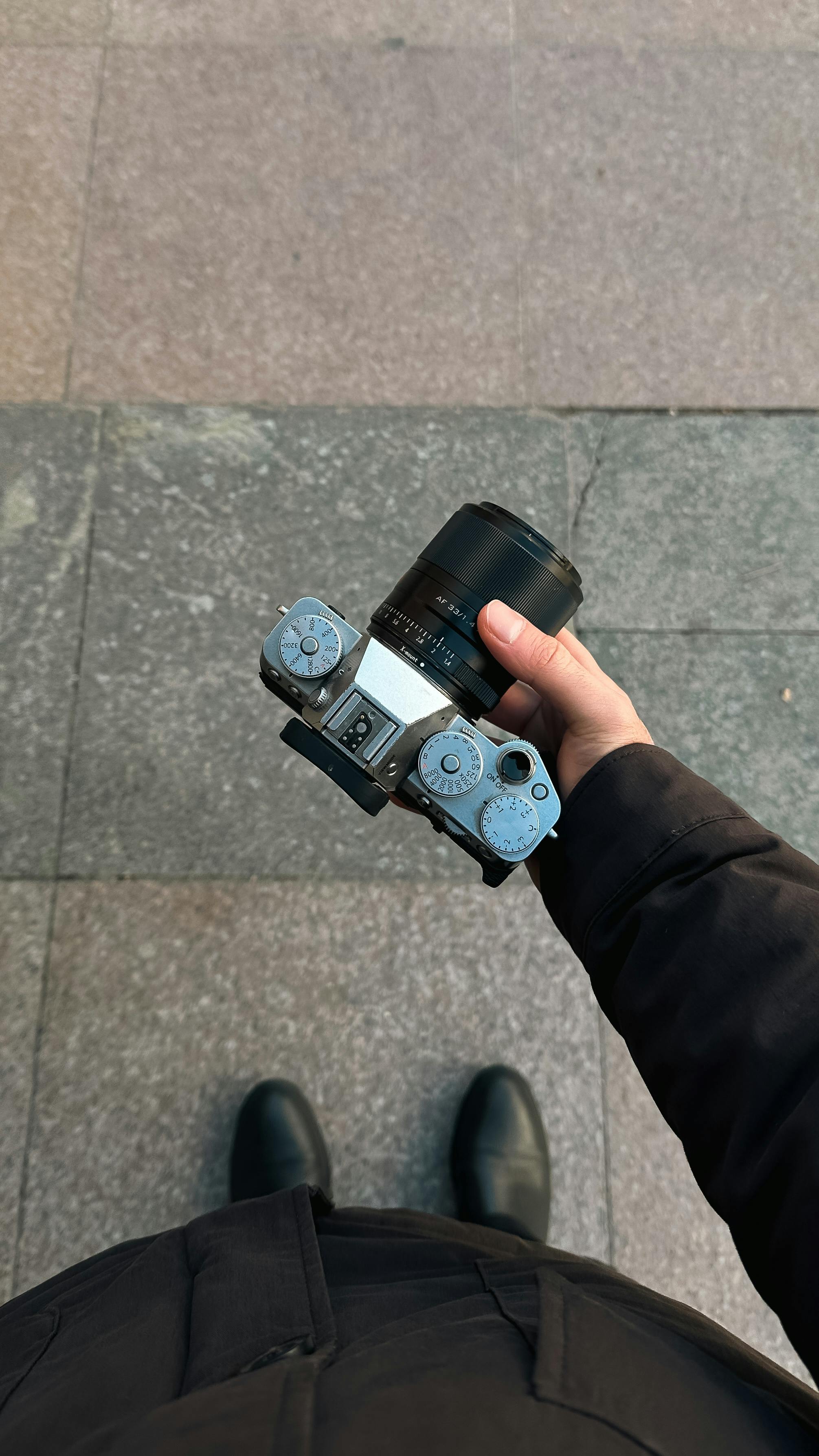 Bezpłatne Osoba trzymająca zabytkowy aparat fotograficzny z perspektywy lotu ptaka na tle kamiennego chodnika. Zdjęcie z galerii