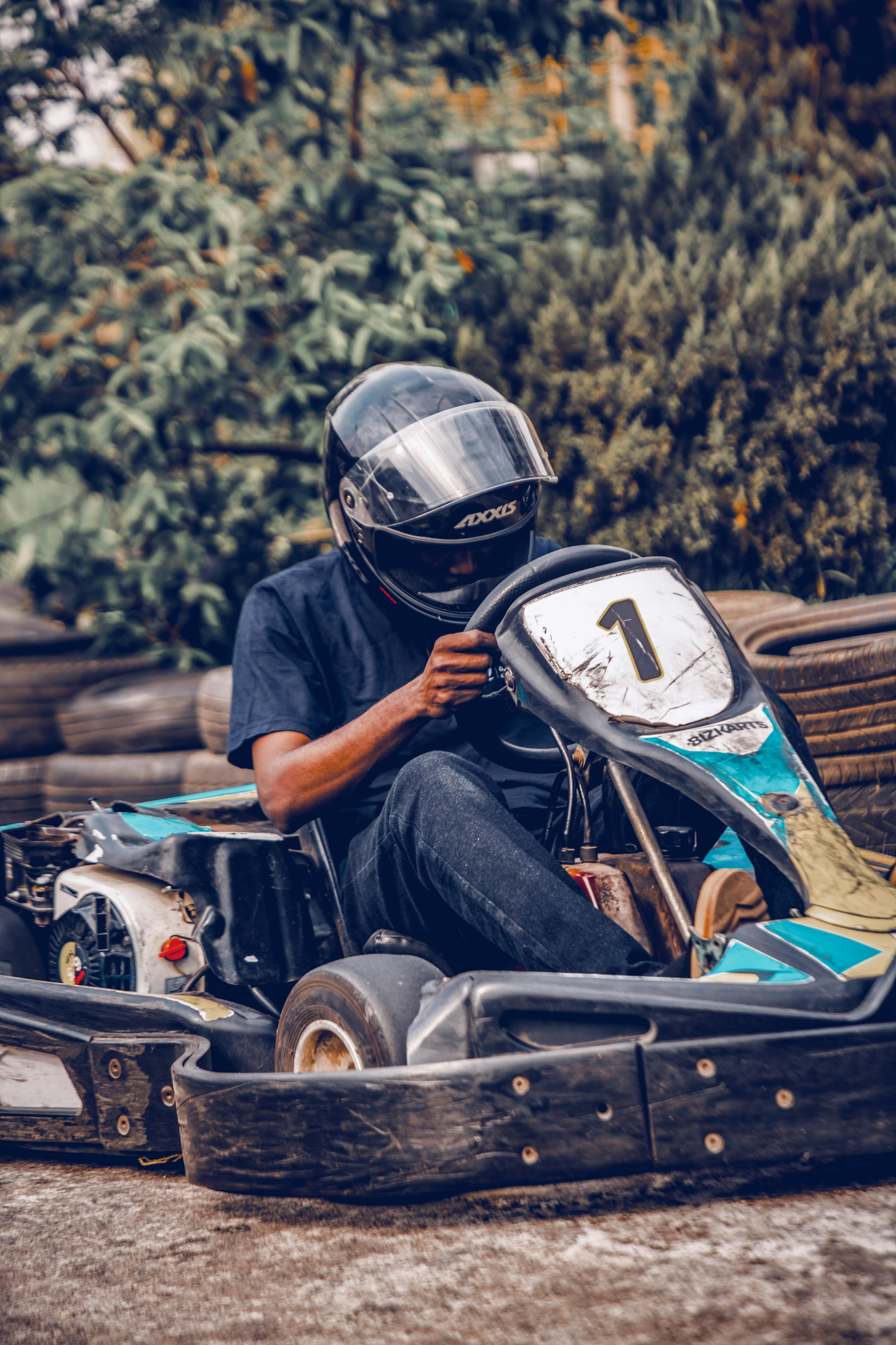 無料 ヘルメットをかぶった男性が、屋外のレーストラックでゴーカートを運転している。 写真素材