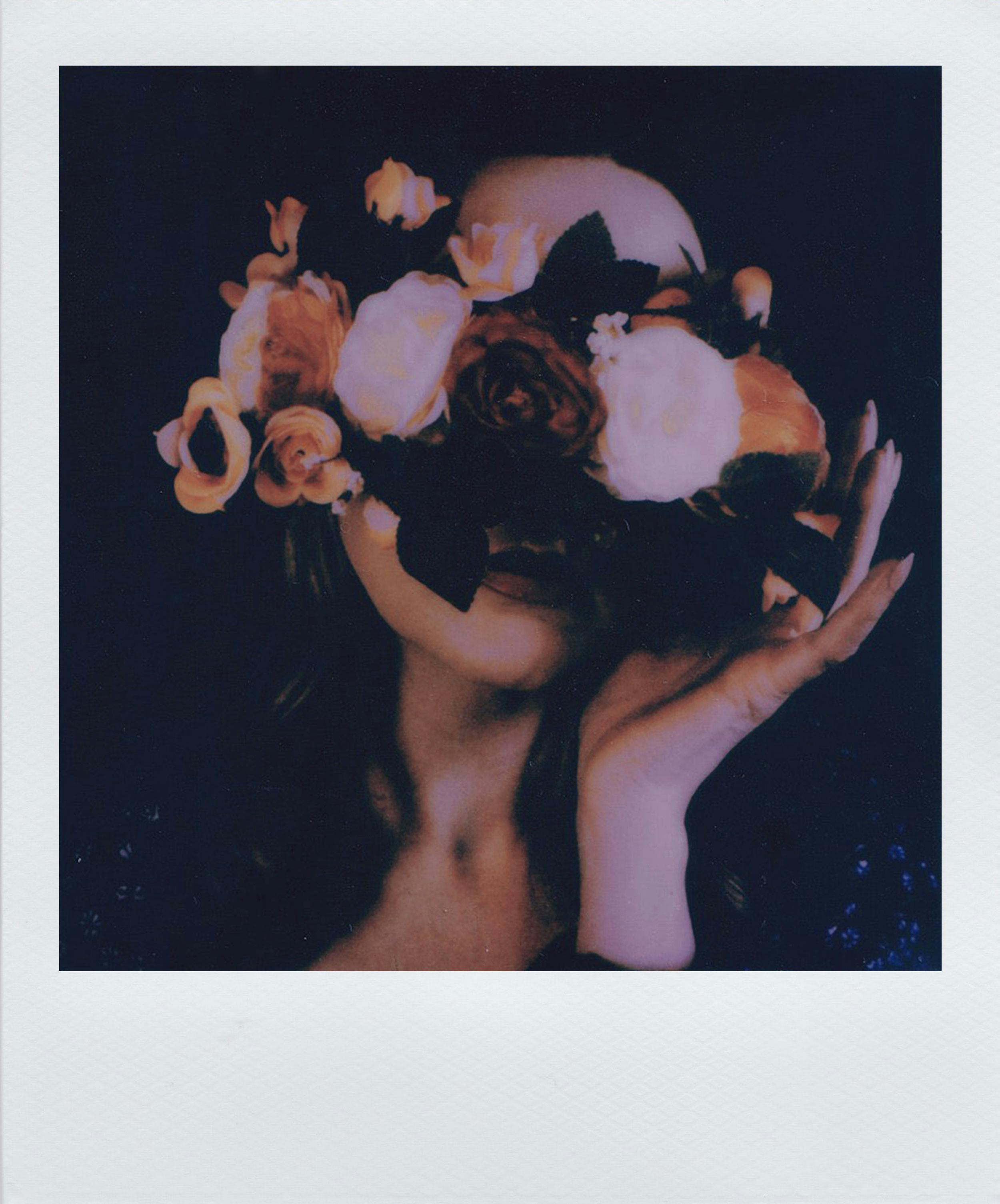 Moody portrait of a woman obscured by vibrant flowers, creating a dramatic and artistic effect.