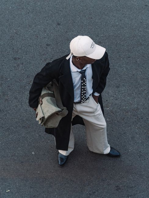 Stylish young man in coat and cap walking on city street viewed from above.