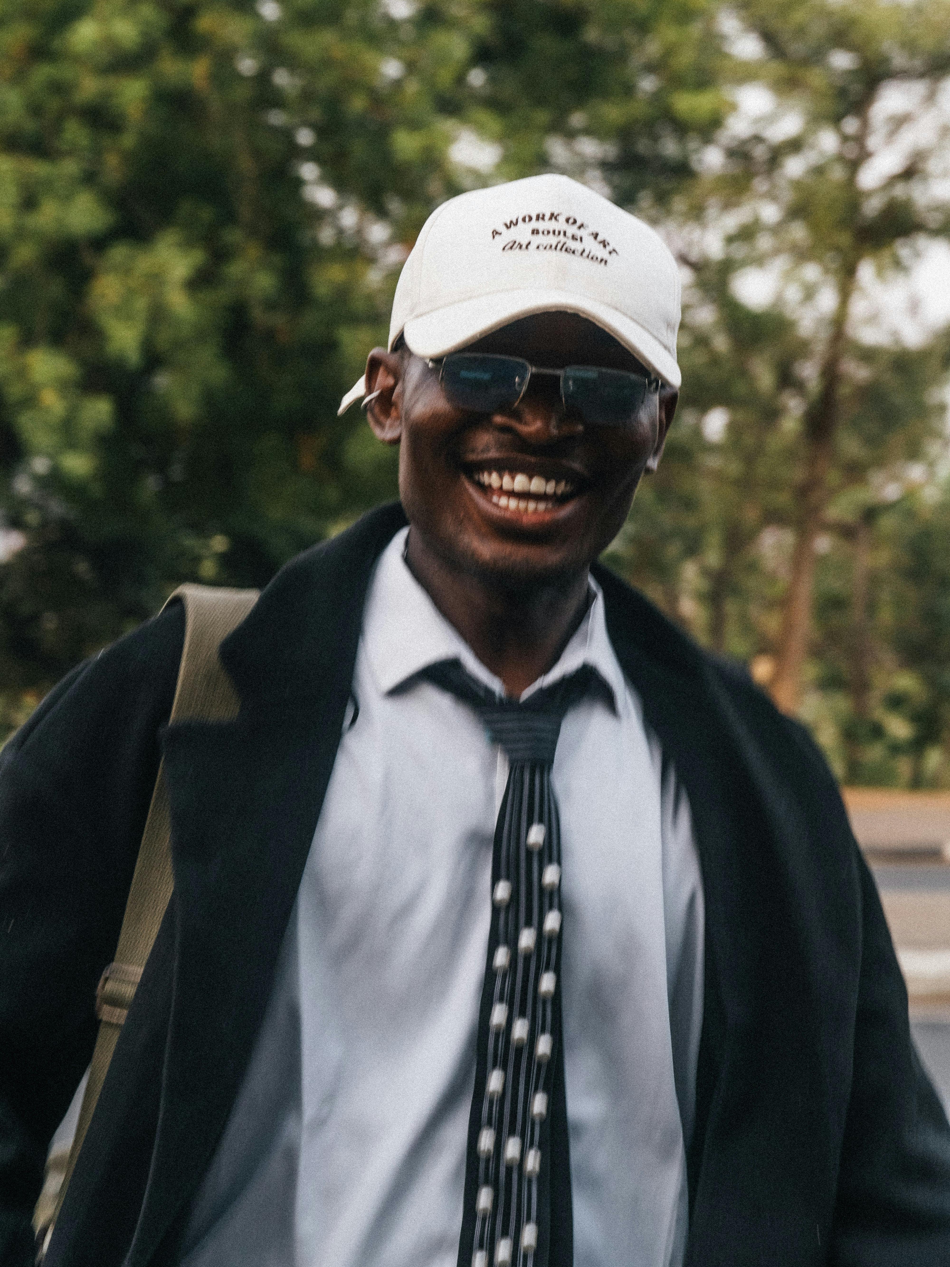 ฟรี ชายหนุ่มมีความสุข สวมแว่นกันแดดและหมวกสีขาว กำลังเพลิดเพลินกับวันดีๆ ข้างนอก คลังภาพถ่าย