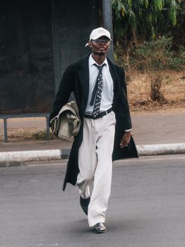 Stylish man in trench coat walking confidently on a street in Abuja, Nigeria.