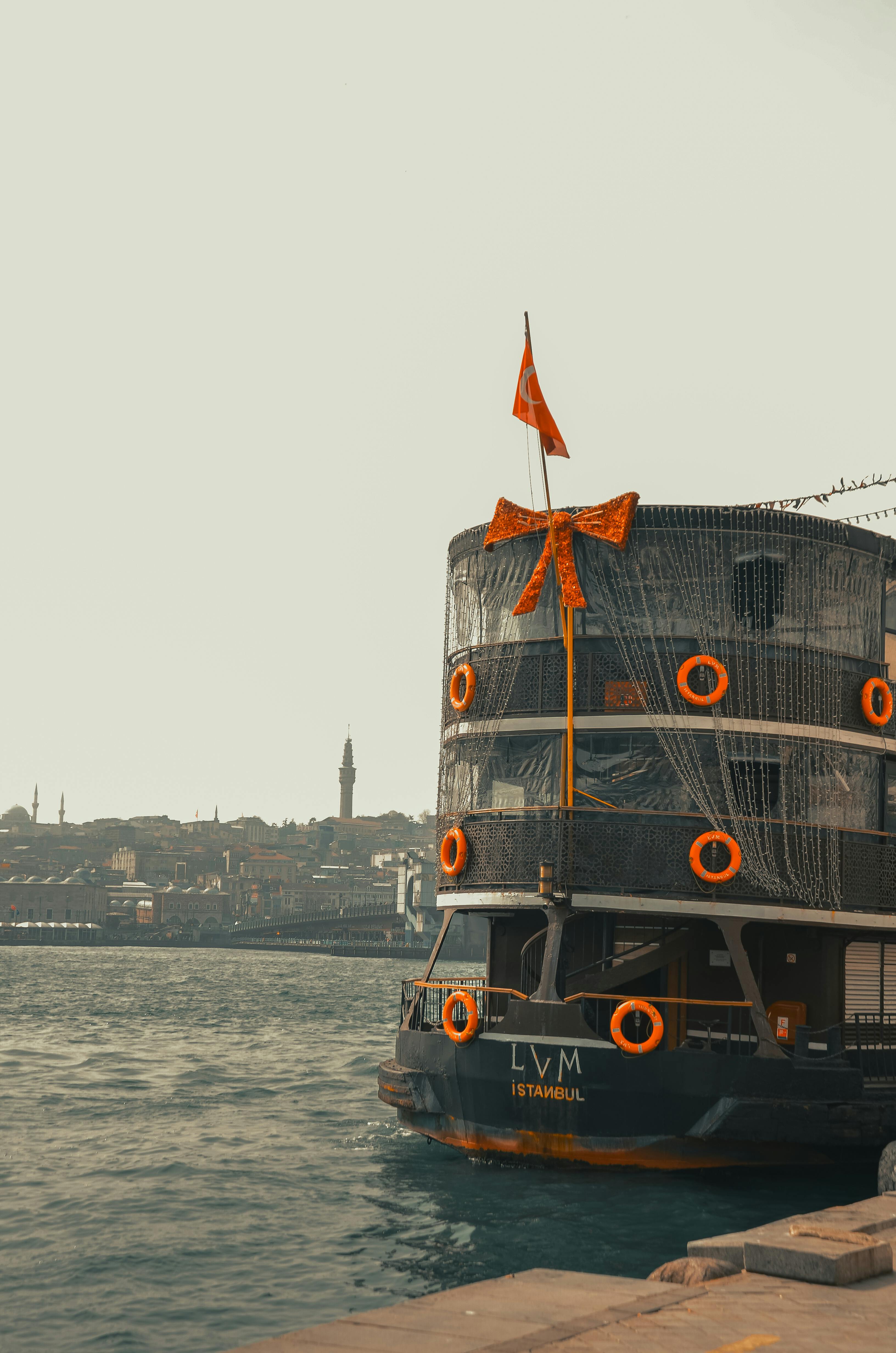 ingyenes Narancssárga díszítéssel díszített ünnepi komp, amely az isztambuli vízparton köt ki, kilátással a városra. Stockfotó