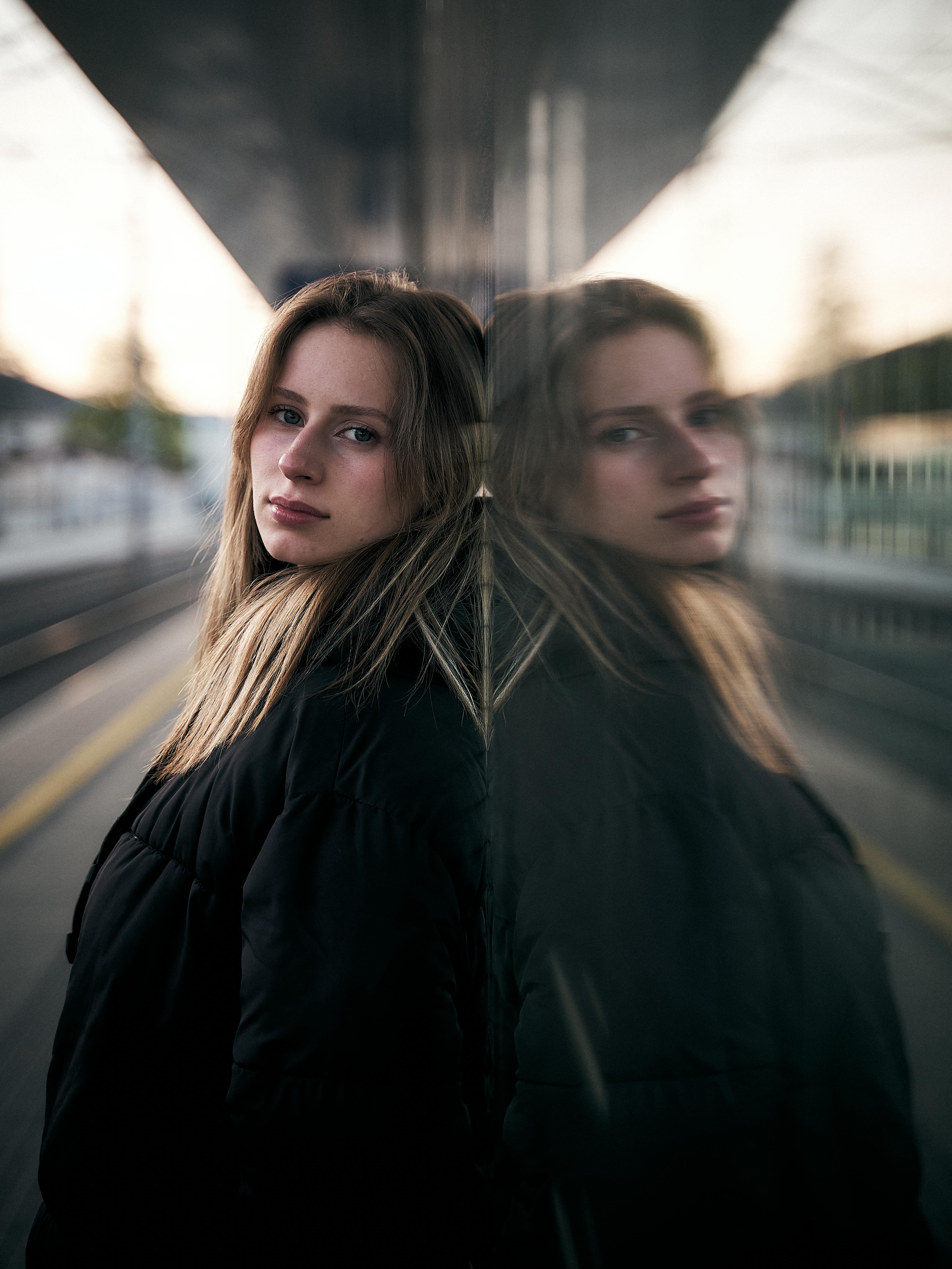 Gratis Una giovane donna fissa l'obiettivo della macchina fotografica, il suo riflesso visibile su una superficie di vetro nella stazione ferroviaria di Leibnitz. Foto a disposizione