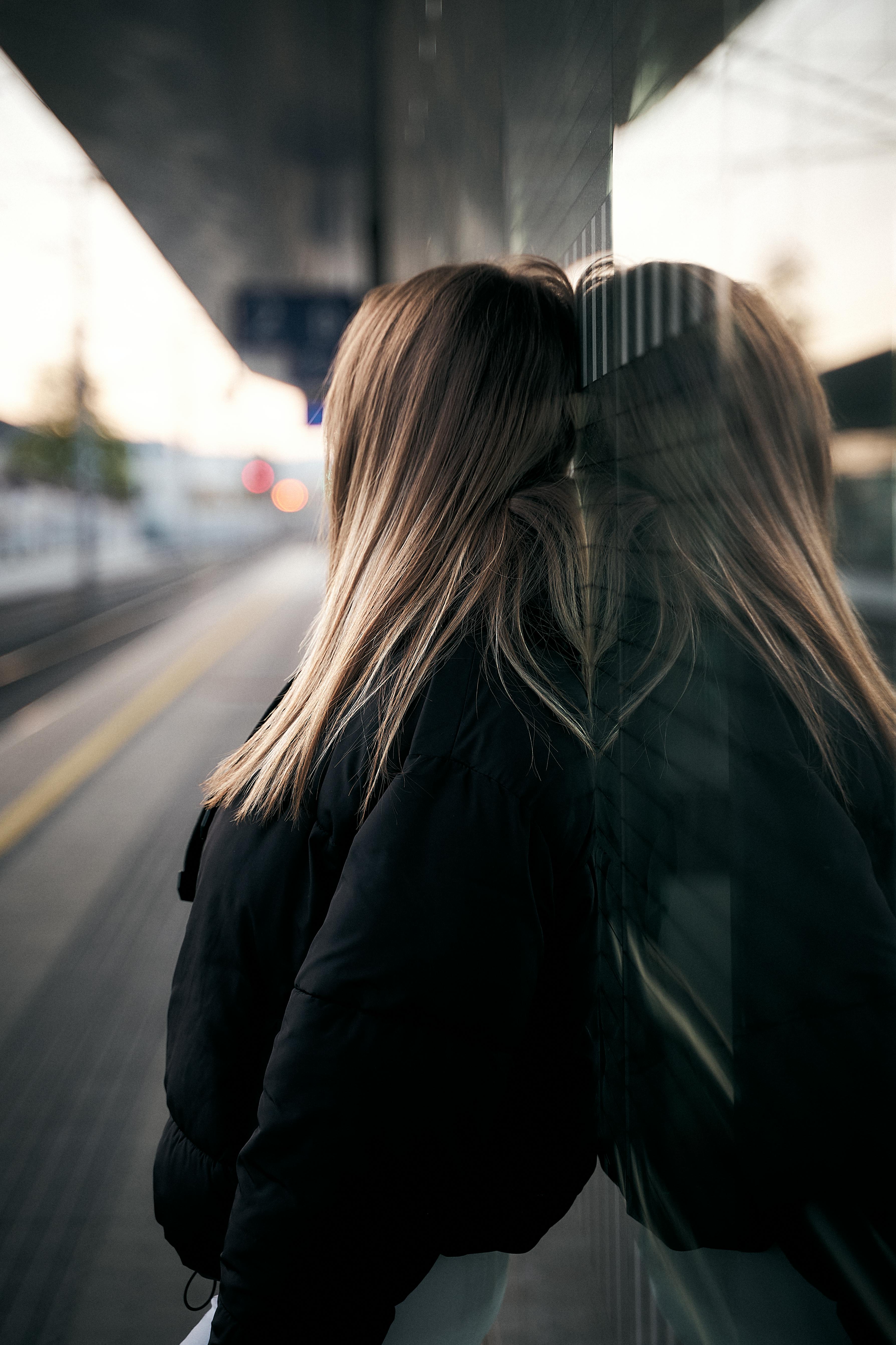 Gratuit Dans une gare autrichienne, une femme s'appuie contre une surface réfléchissante, l'air pensif. Photos