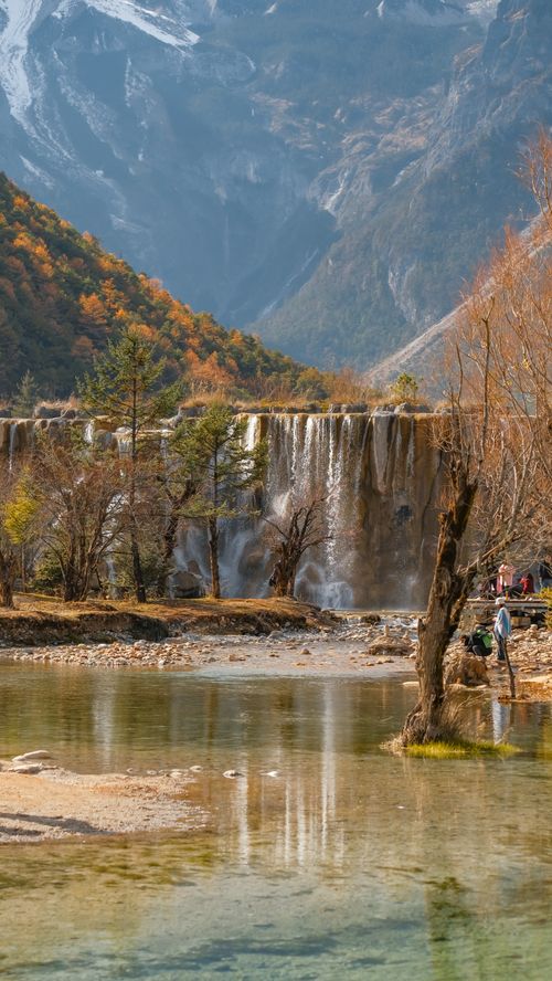Free Beautiful autumn view of a waterfall surrounded by colorful trees in Lijiang, China. Stock Photo