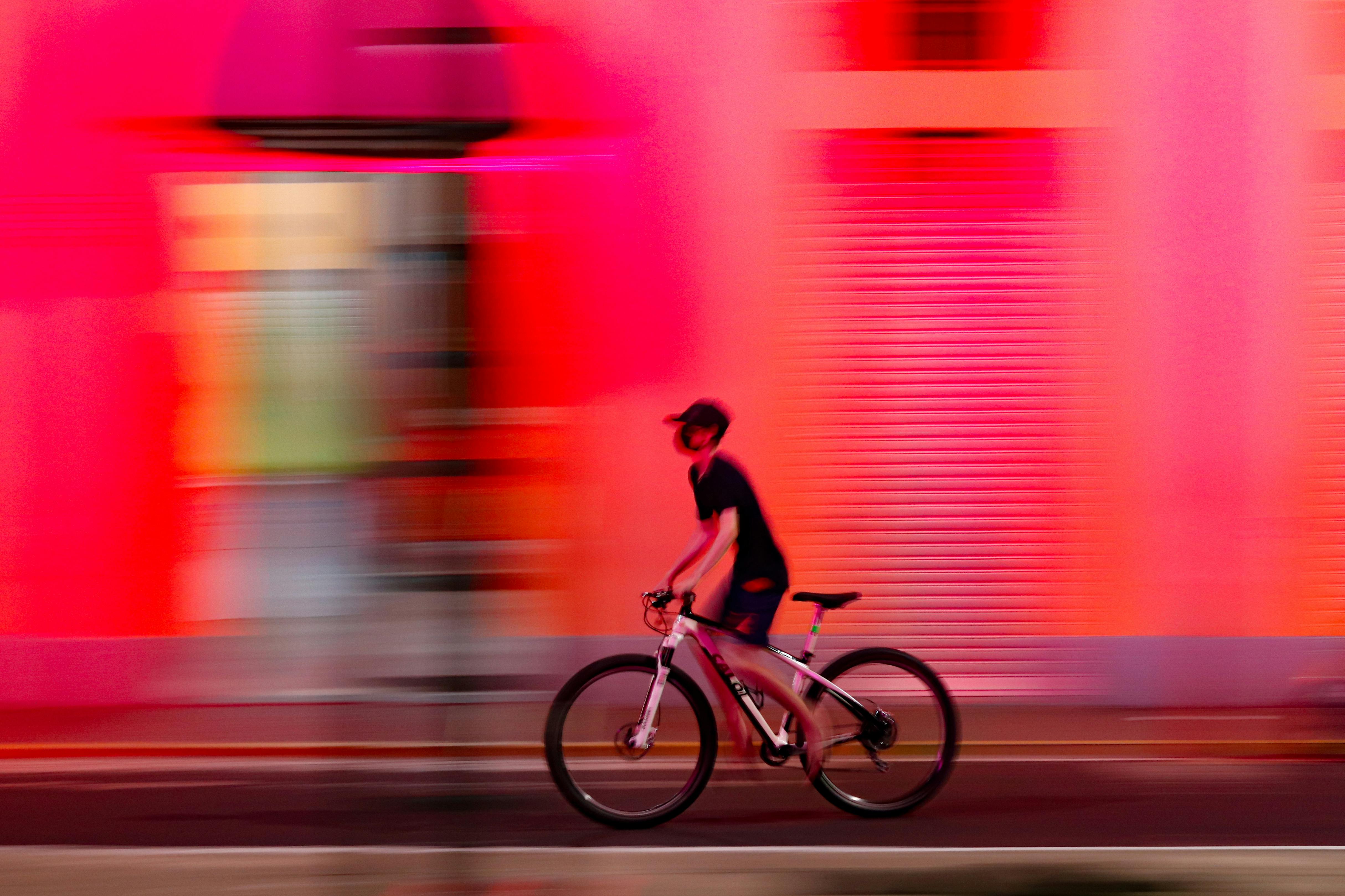 無料 ブラジルのパリンティンスで、自転車に乗った人が鮮やかな色の建物を素早く通り過ぎていく。都市の動きが残像となって際立つ光景だ。 写真素材