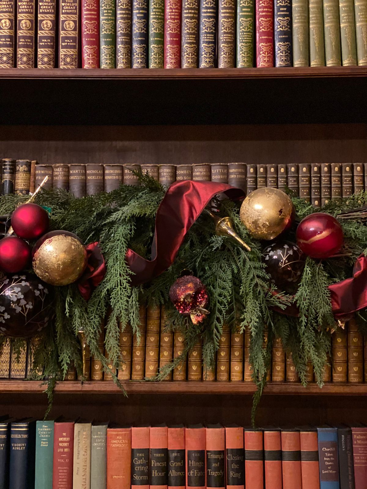 Christmas garland with red and gold ornaments draped along a wooden bookshelf full of old books