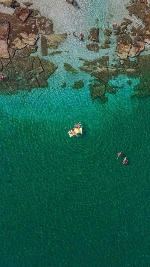 Free Aerial view of people swimming and relaxing in clear, turquoise sea waters with rocky shorelines. Stock Photo
