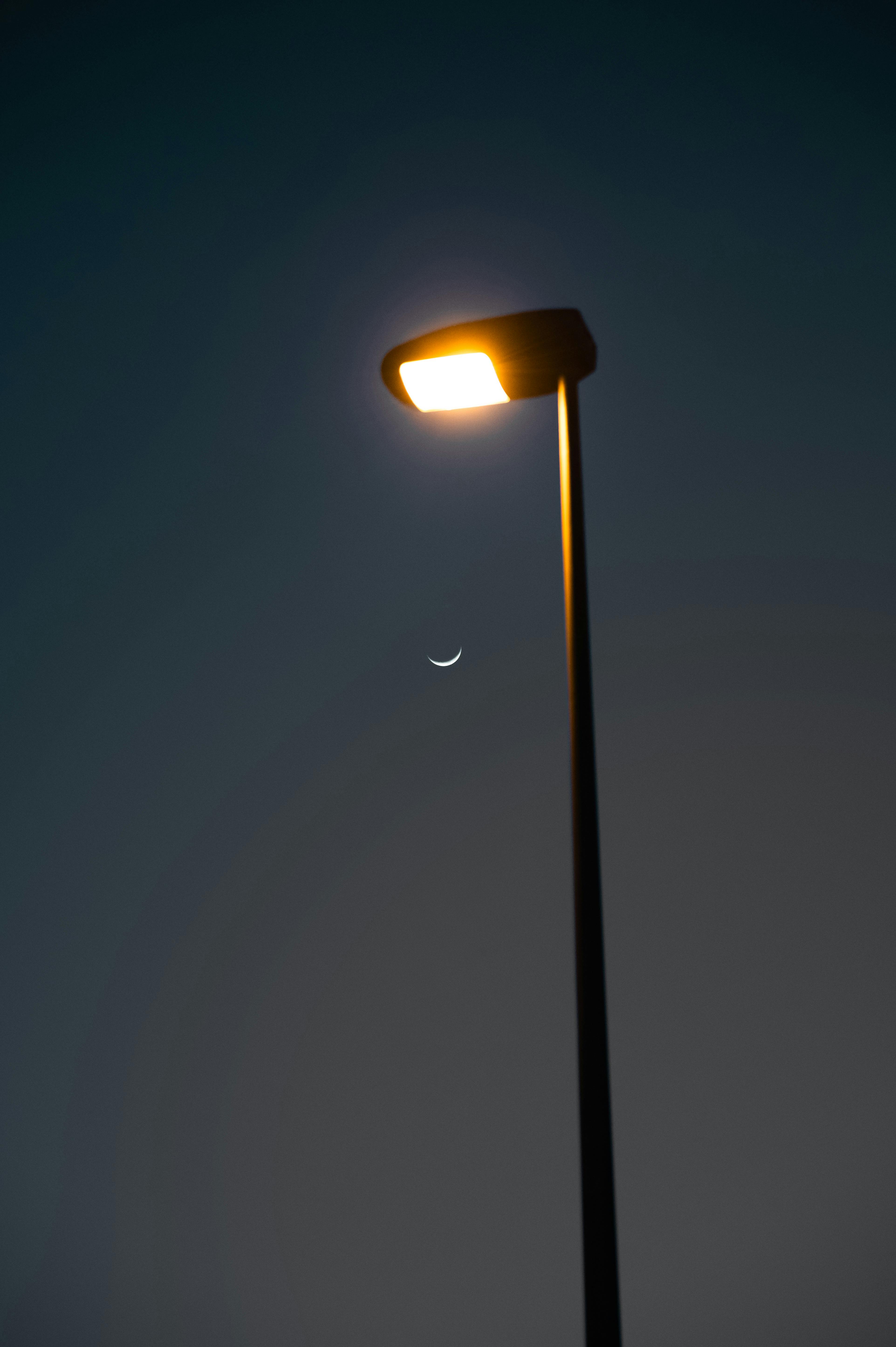 Bezpłatne Światło latarni ulicznej obok półksiężyca na nocnym niebie tworzy spokojną, miejską atmosferę. Zdjęcie z galerii