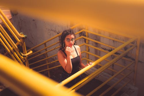 Woman in Black Tank Top and Black Pants Standing on Yellow Metal Staircase